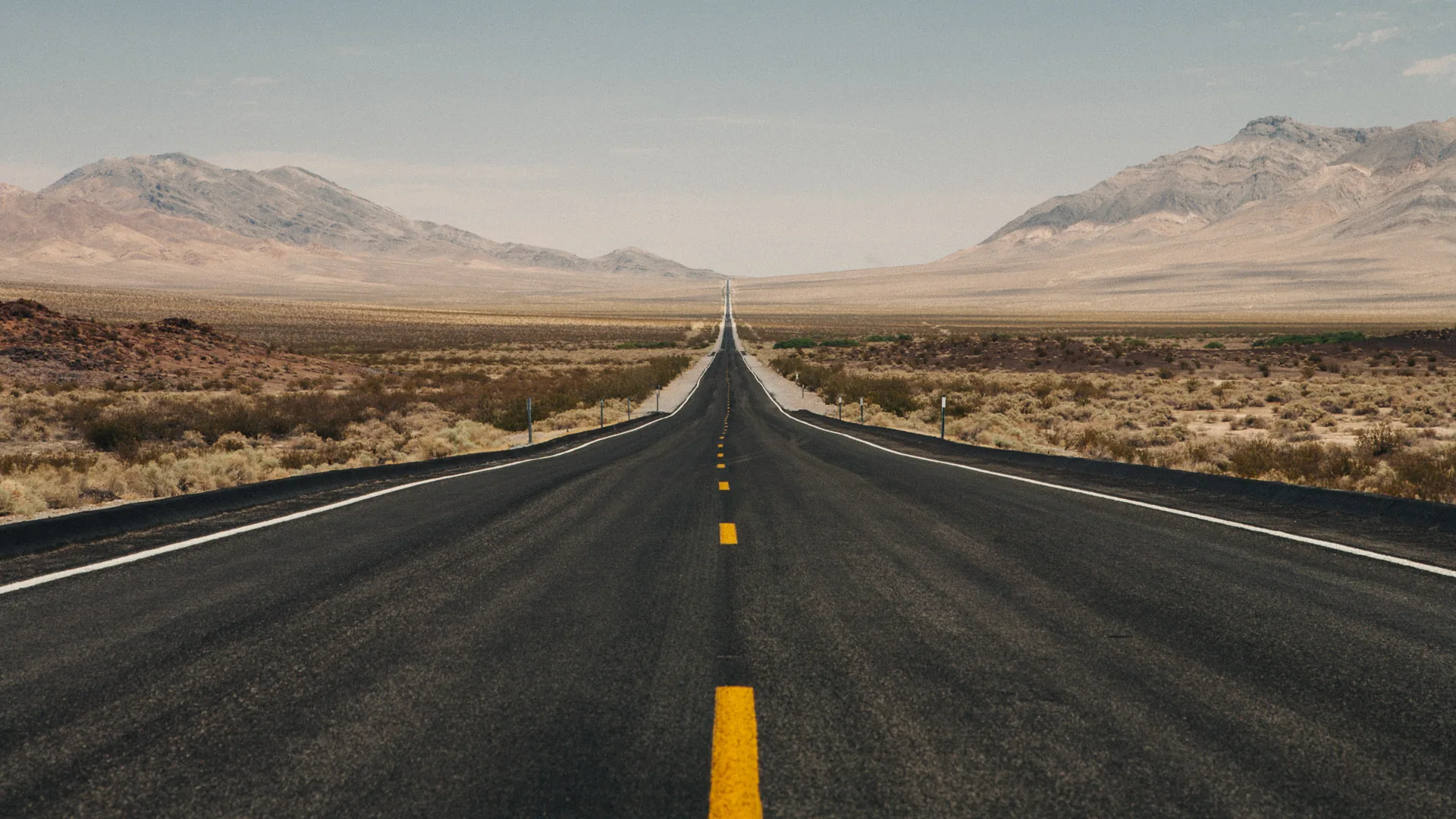 A straight empty road running between bare mountains into Death Valley