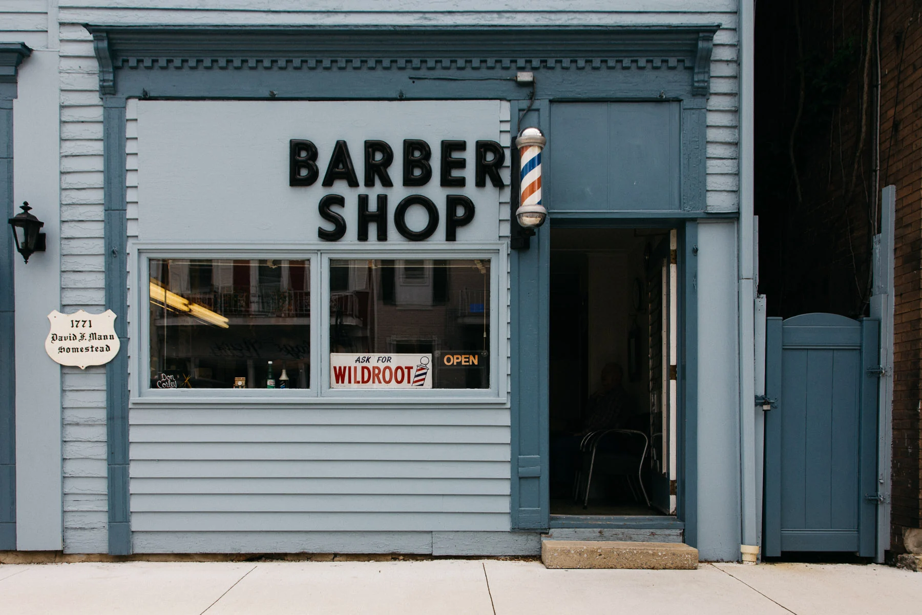 The pale blue front of a small barber shop with a striped pole