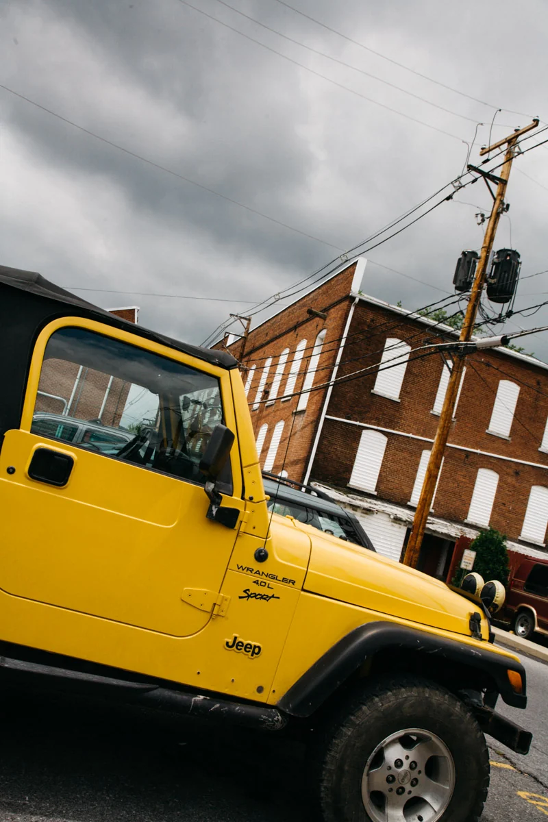 A yellow Jeep parked below a brick building and power lines
