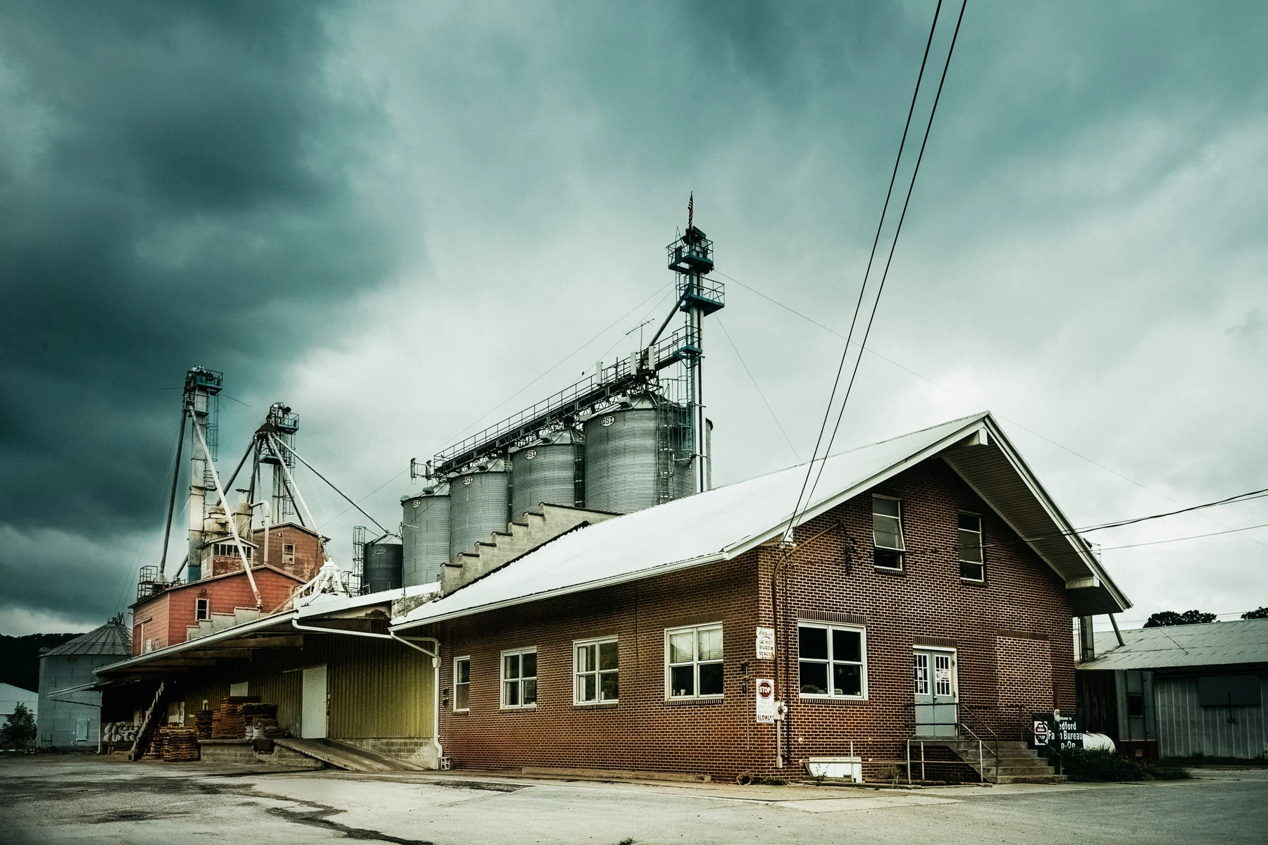 A brick grain elevator and silos beneath dark storm clouds