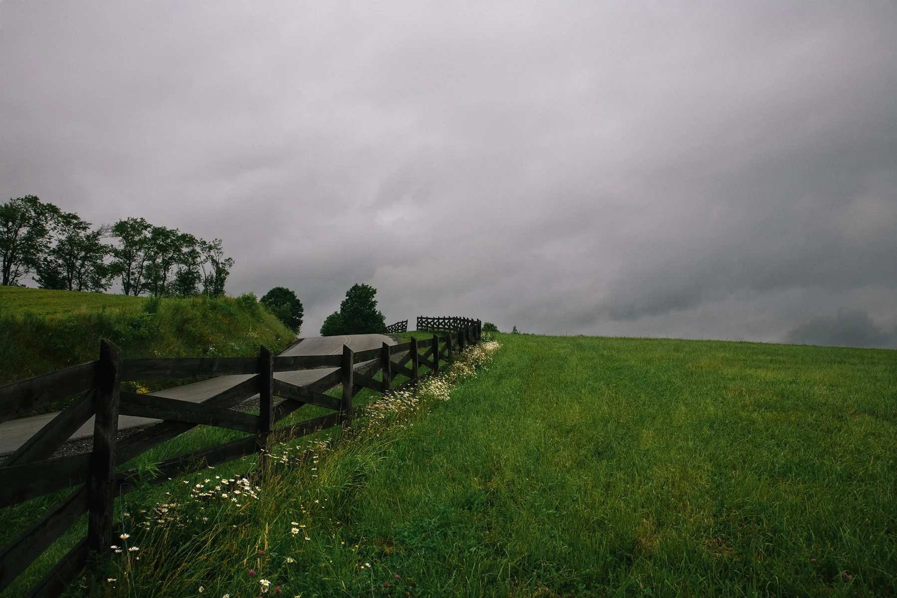 A wooden fence running along a grassy hillside under a stormy sky