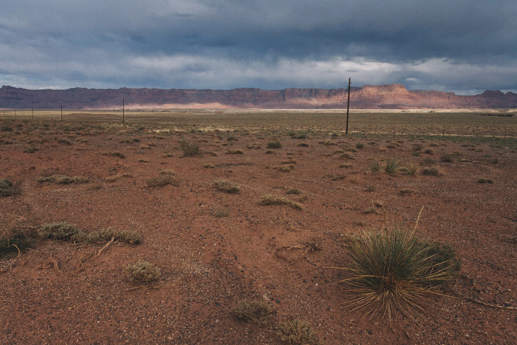 Red desert and the distant cliffs under a dark sky