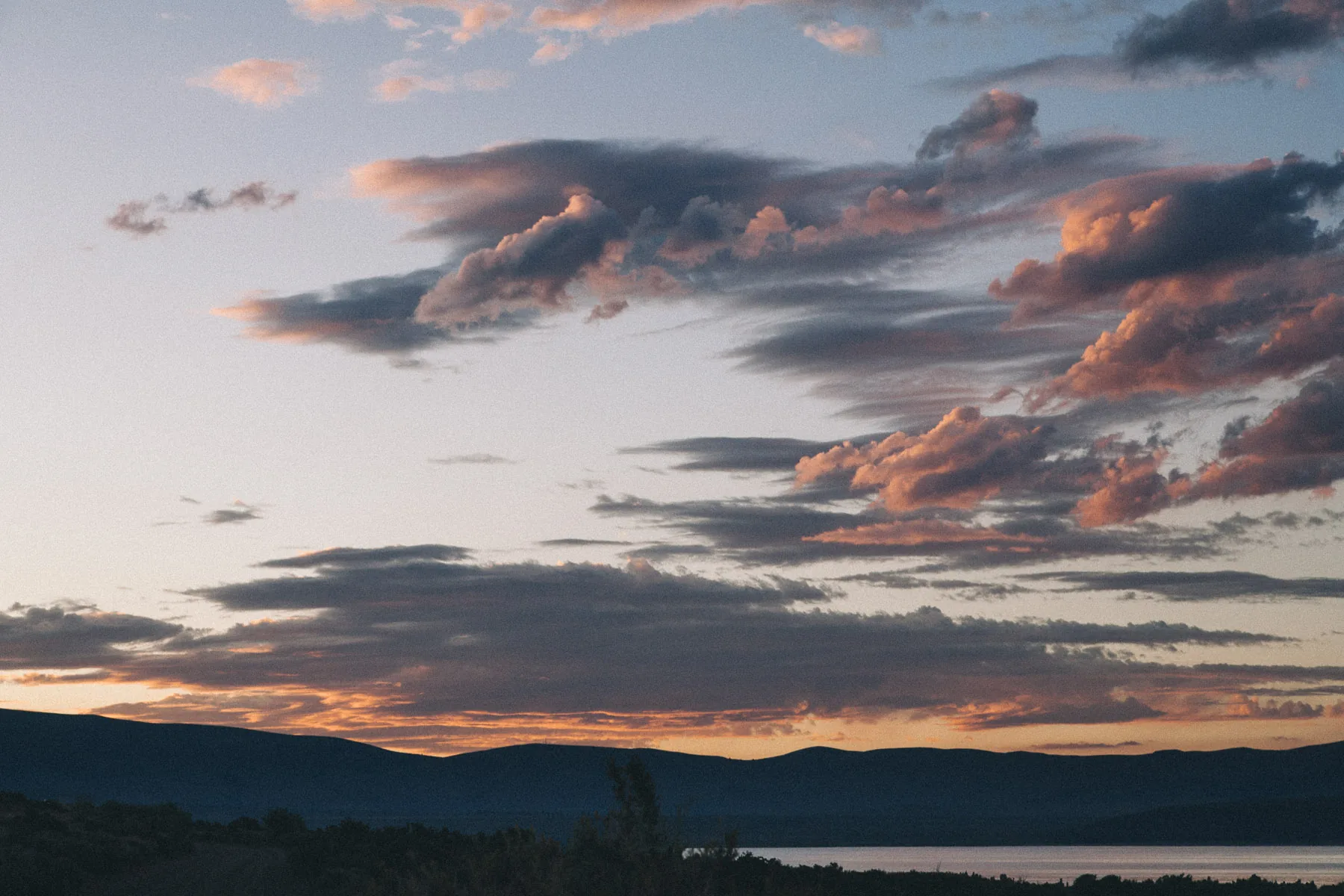 Pink clouds drifting over the dark hills at dusk
