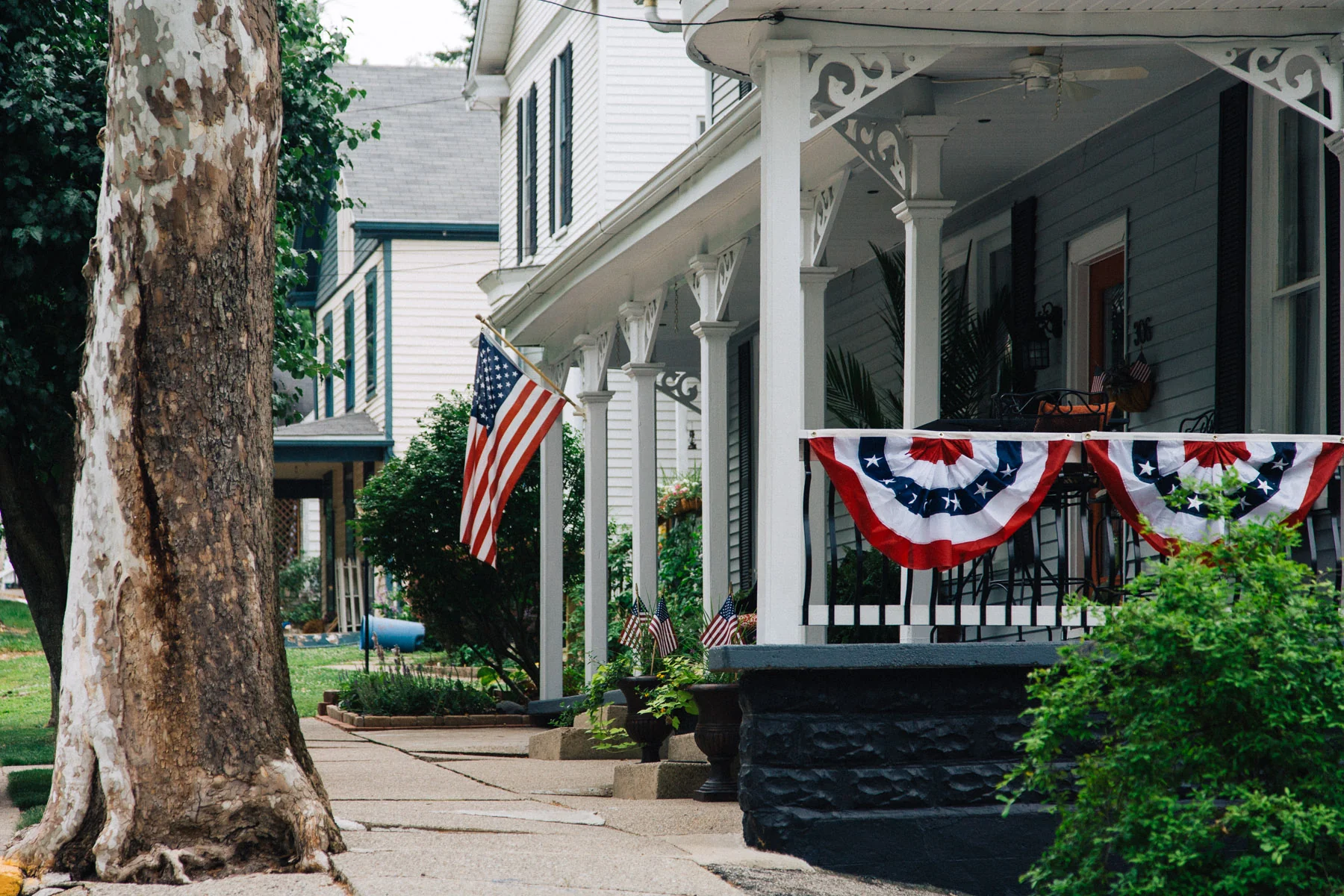 A white porch decorated with flags and bunting behind a pale tree trunk