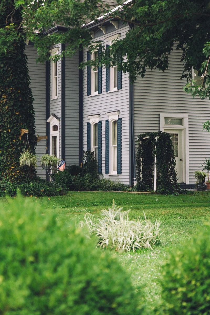 A grey clapboard house behind a lush garden