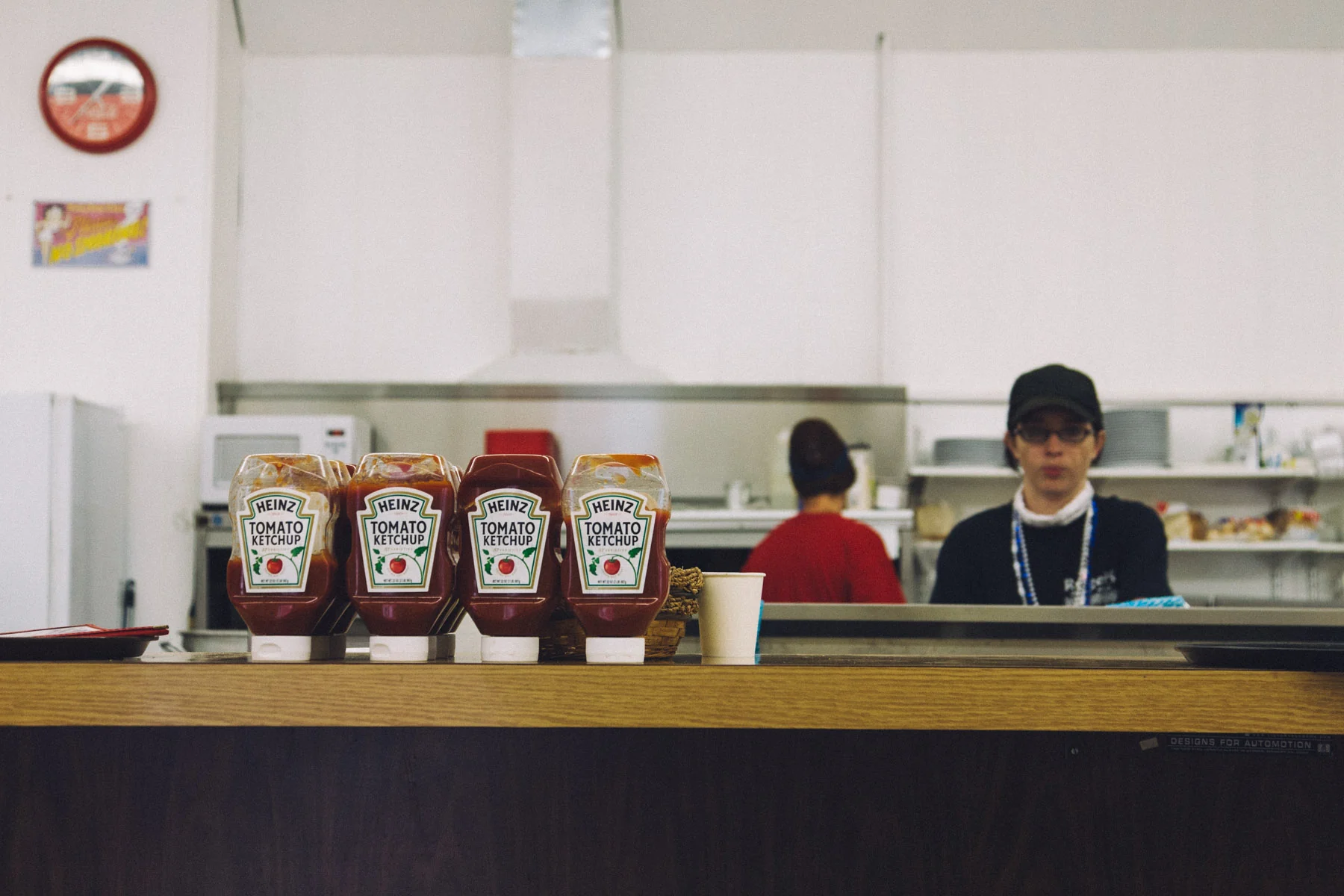 The counter of a small diner with ketchup bottles and a cook