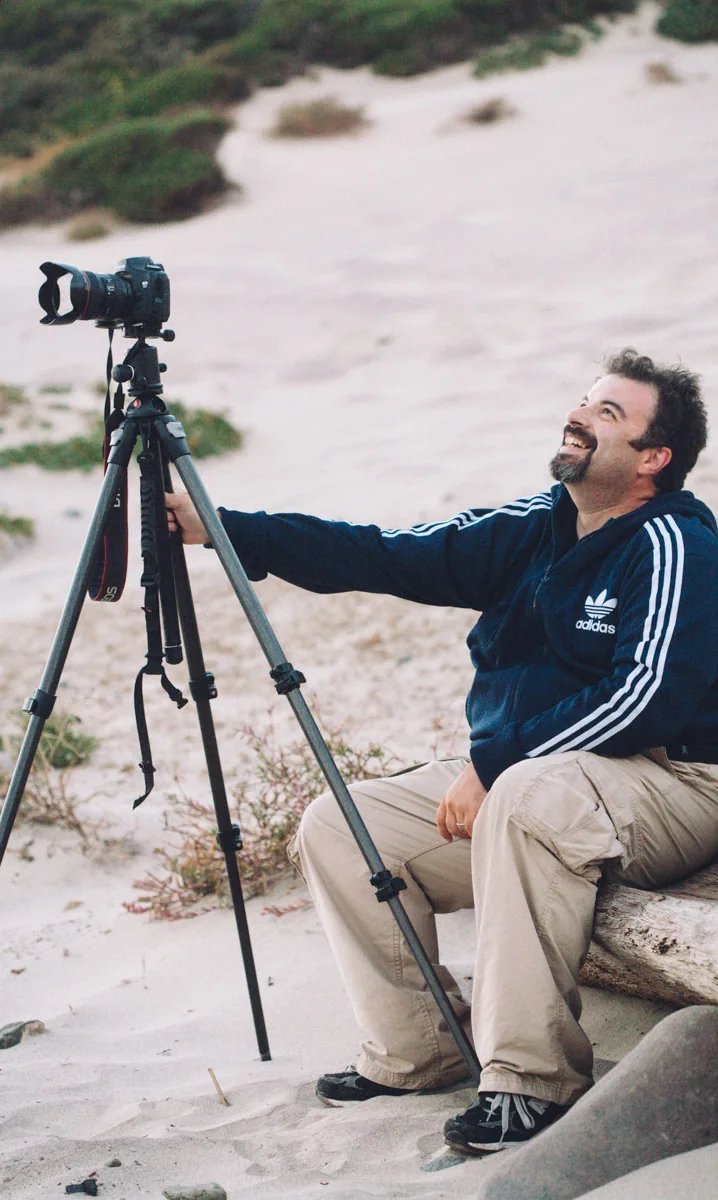 A photographer with his camera on a tripod, sitting on the beach