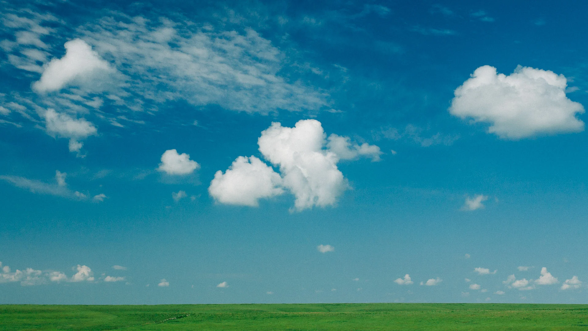 Small white clouds over a flat green horizon