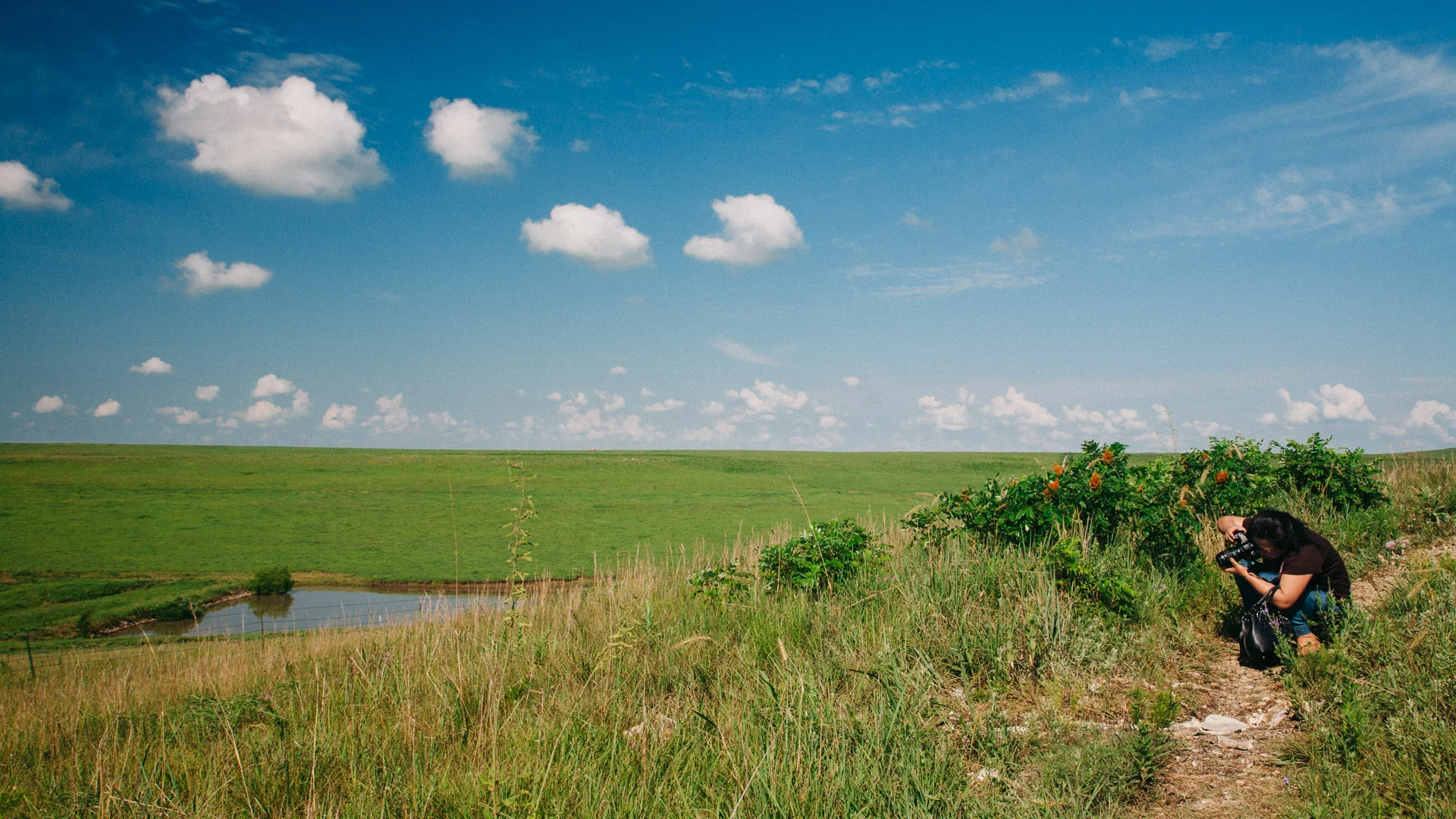 Francesco crouching with his camera on a grassy slope above a pond