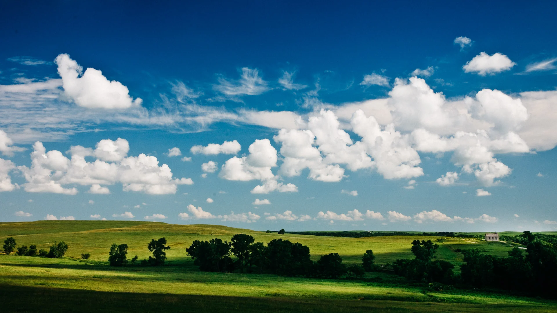 Rolling green prairie under a blue sky scattered with white clouds
