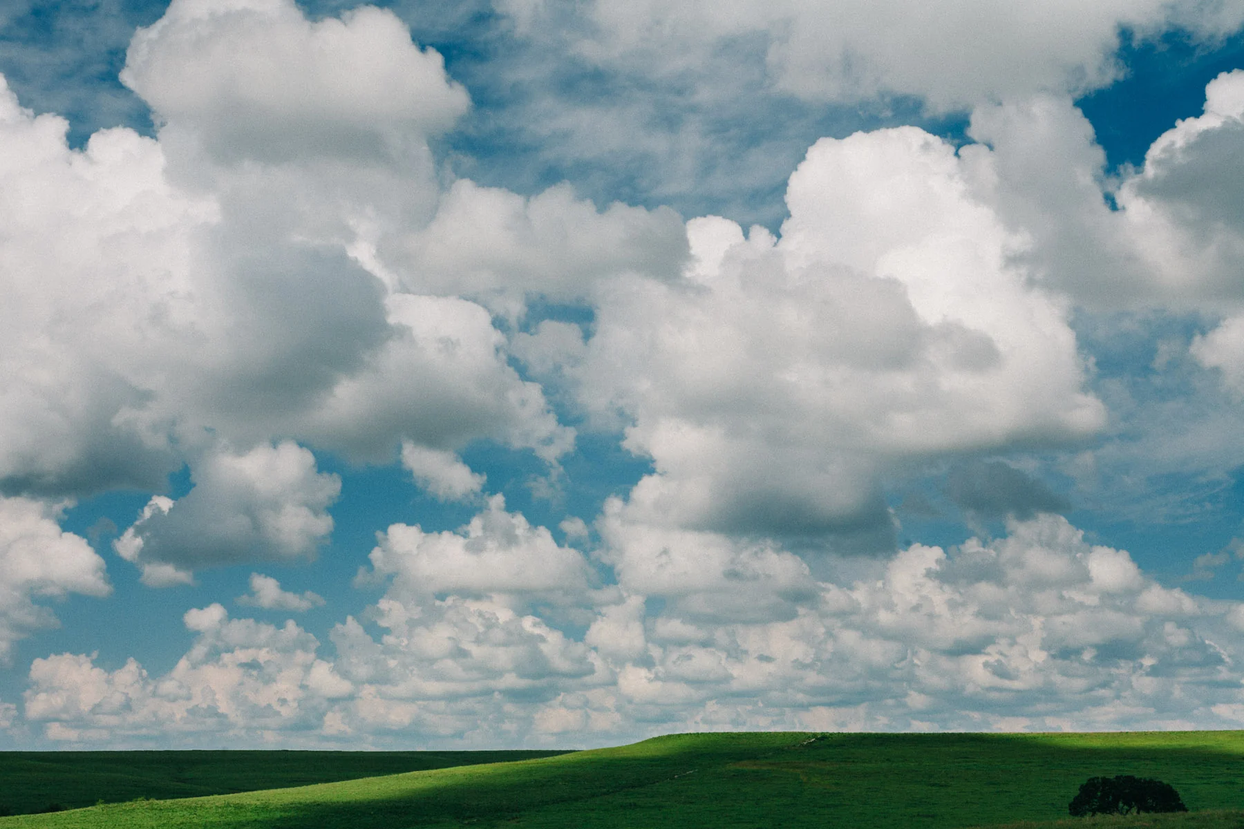 Towering white clouds above a green prairie ridge