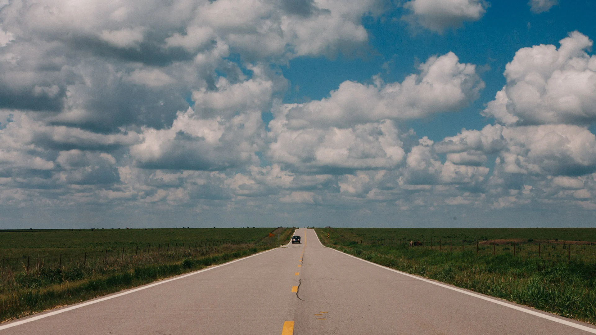 A straight empty road across the plains under heavy clouds