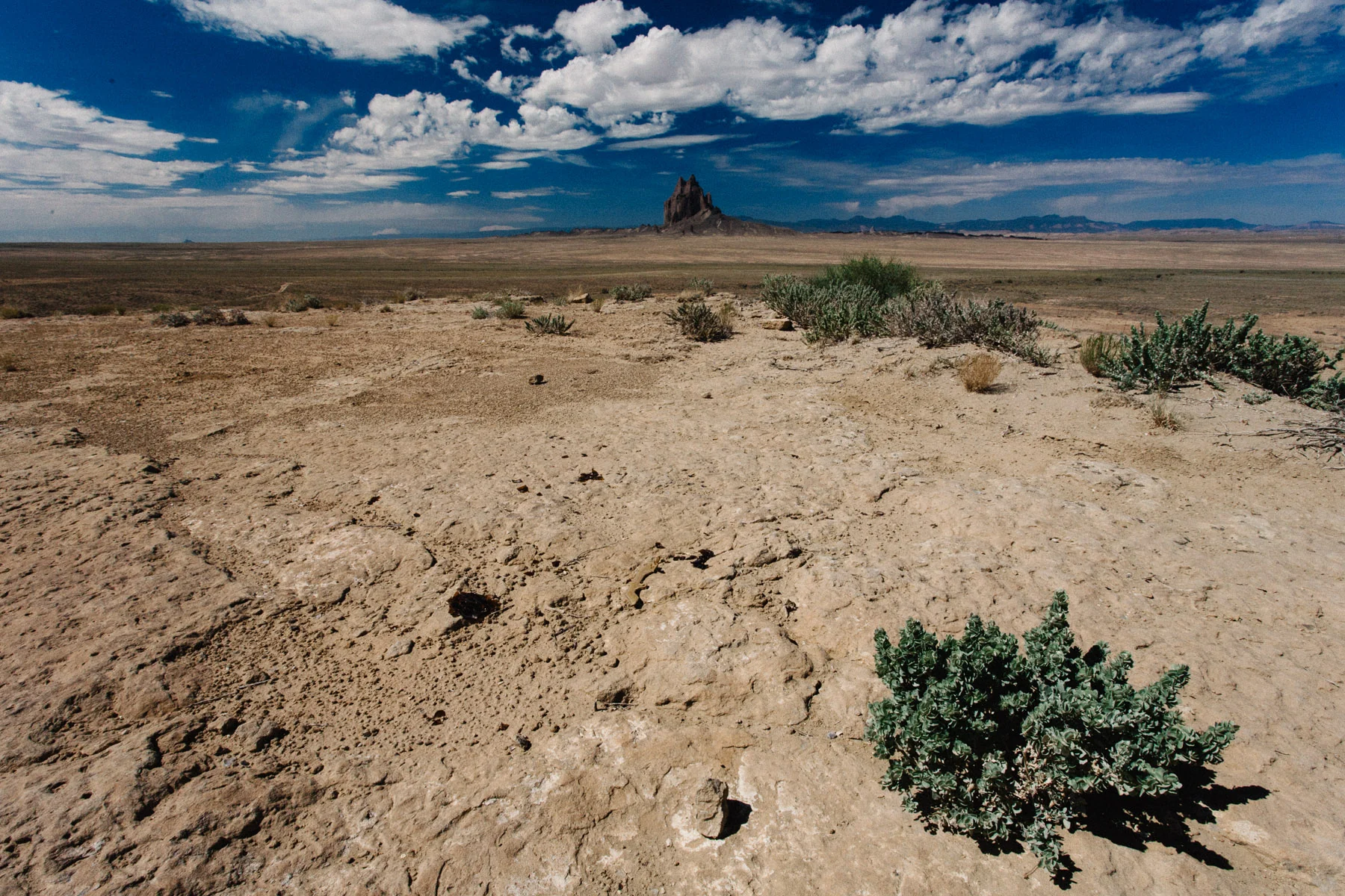 Dry sandy ground with Shiprock far in the distance