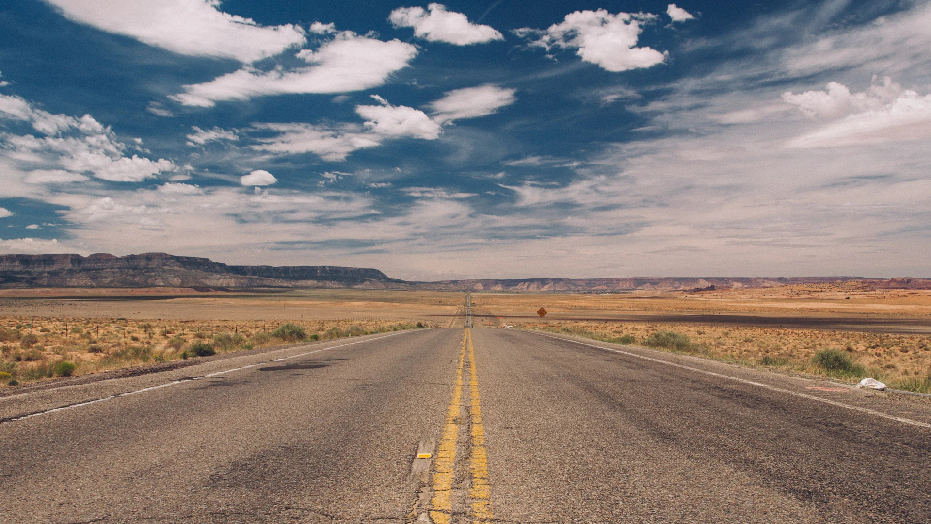A straight desert road under scattered clouds
