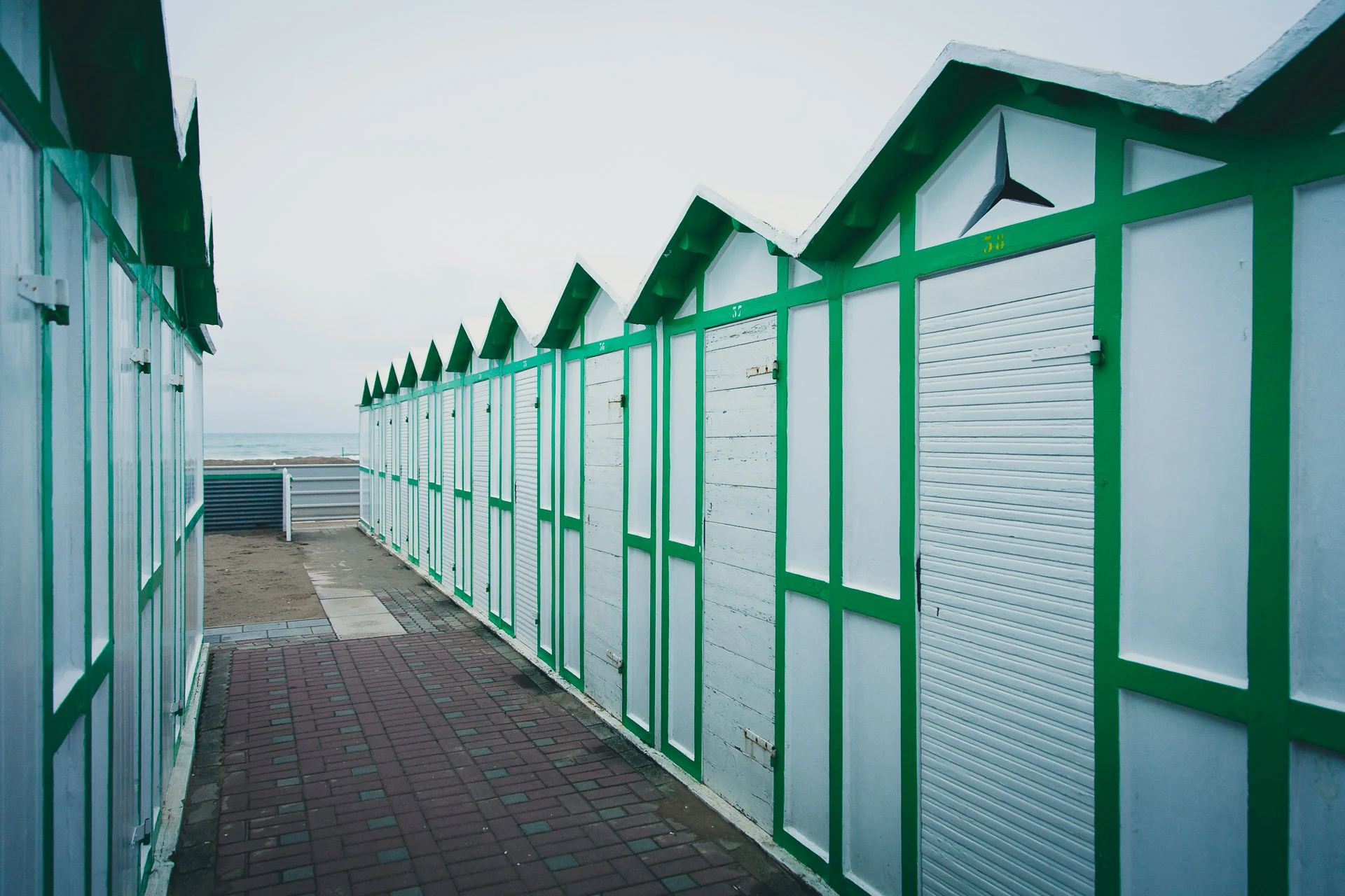 Green and white beach cabins along an empty walkway