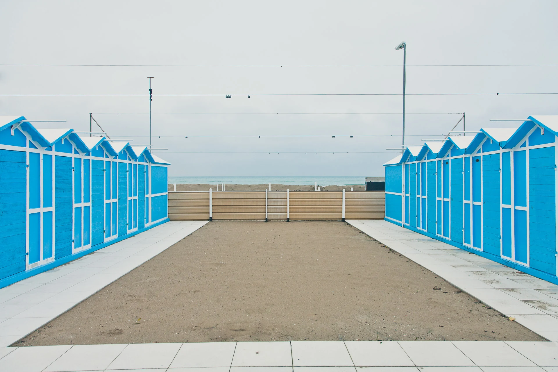Blue beach cabins framing a walkway toward the grey Adriatic Sea