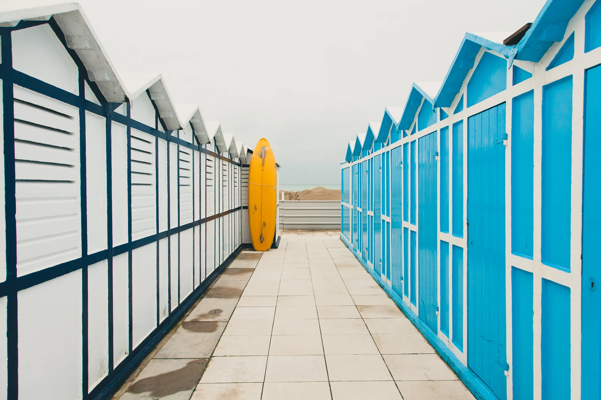 A closed yellow umbrella between rows of blue cabins