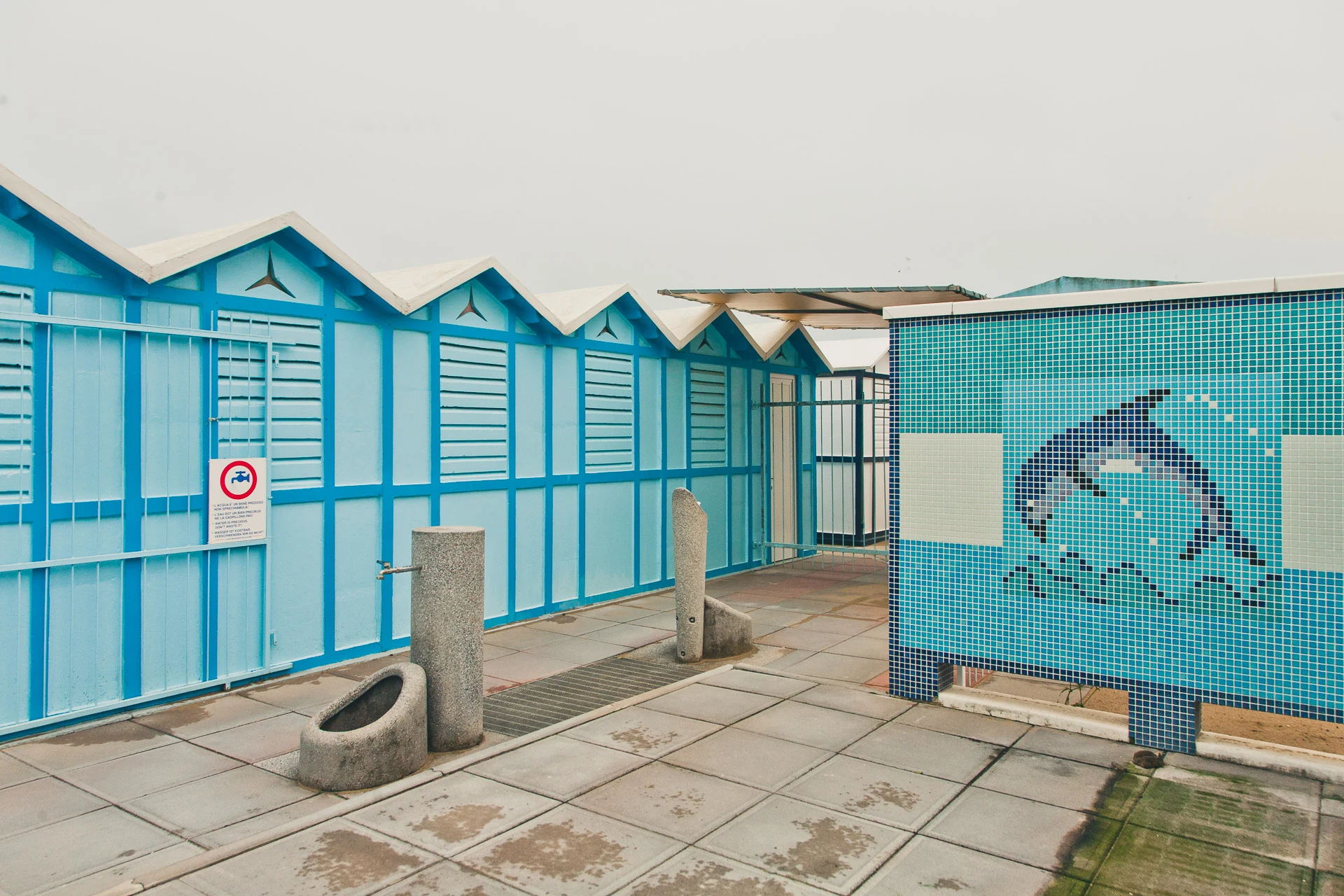 Closed blue beach cabins beside a dolphin mosaic