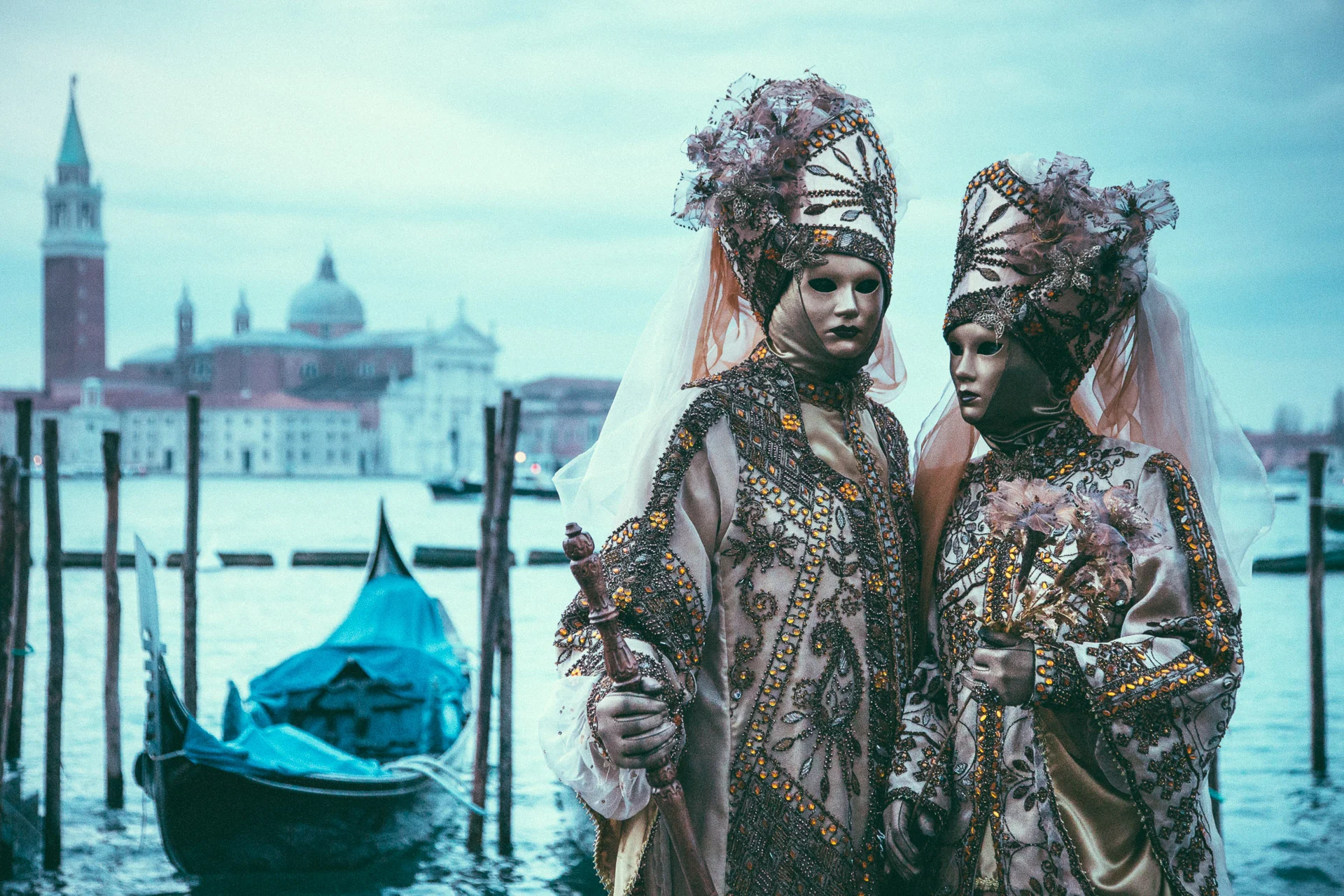 Two masked carnival figures in jewelled costumes beside a gondola, San Giorgio Maggiore behind