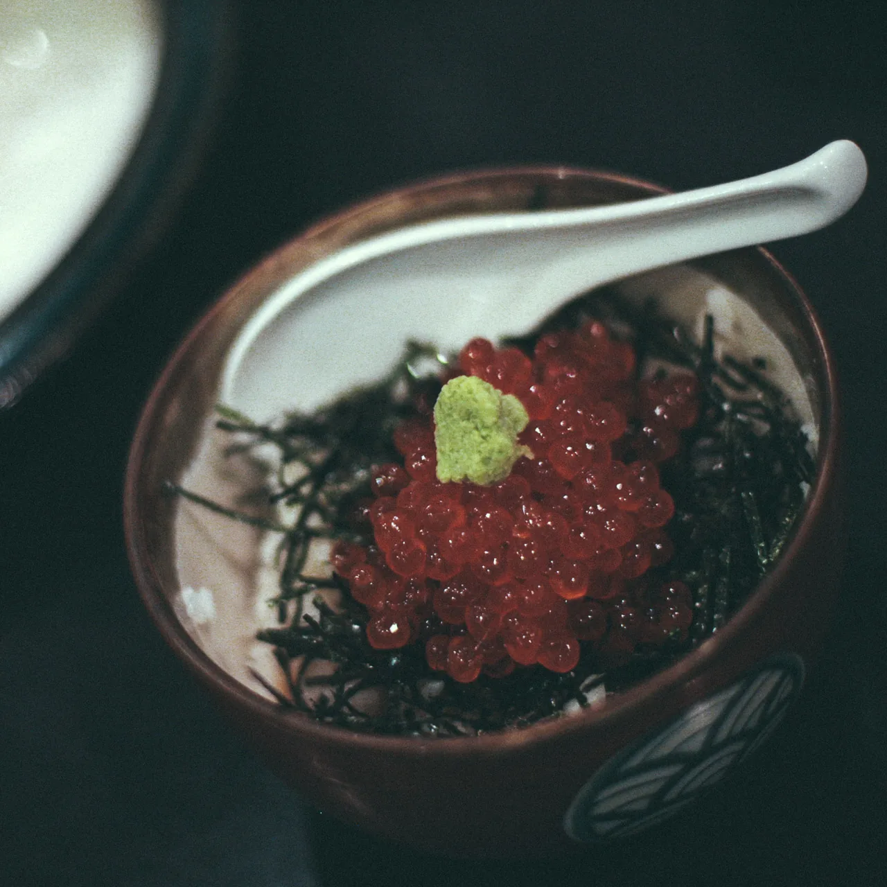 A bowl of ikura on rice and seaweed with a porcelain spoon