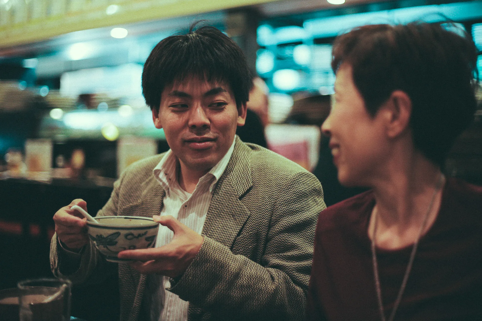 Lifting a bowl to drink, while the conversation goes on
