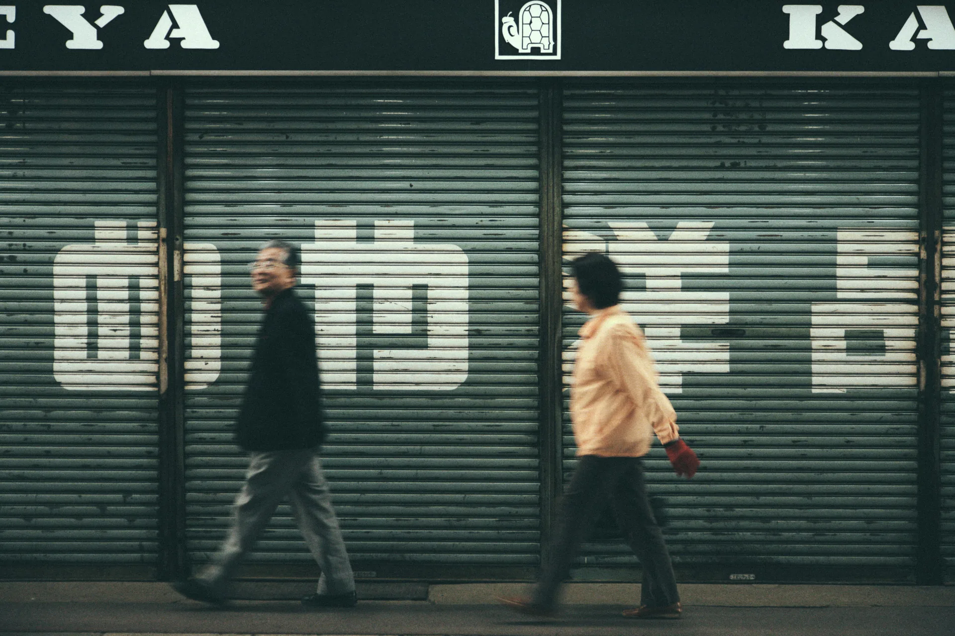 Two people walking past a shuttered shop front in Takayama