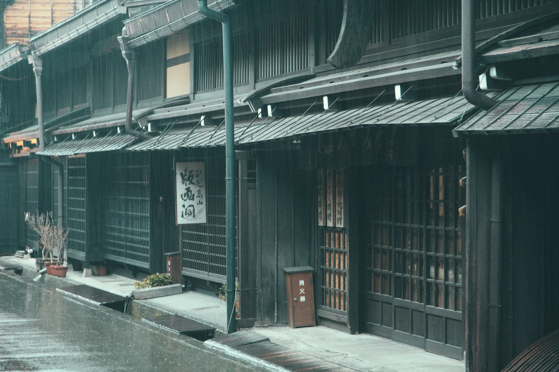 A dark wooden merchant house with lattice windows in the rain