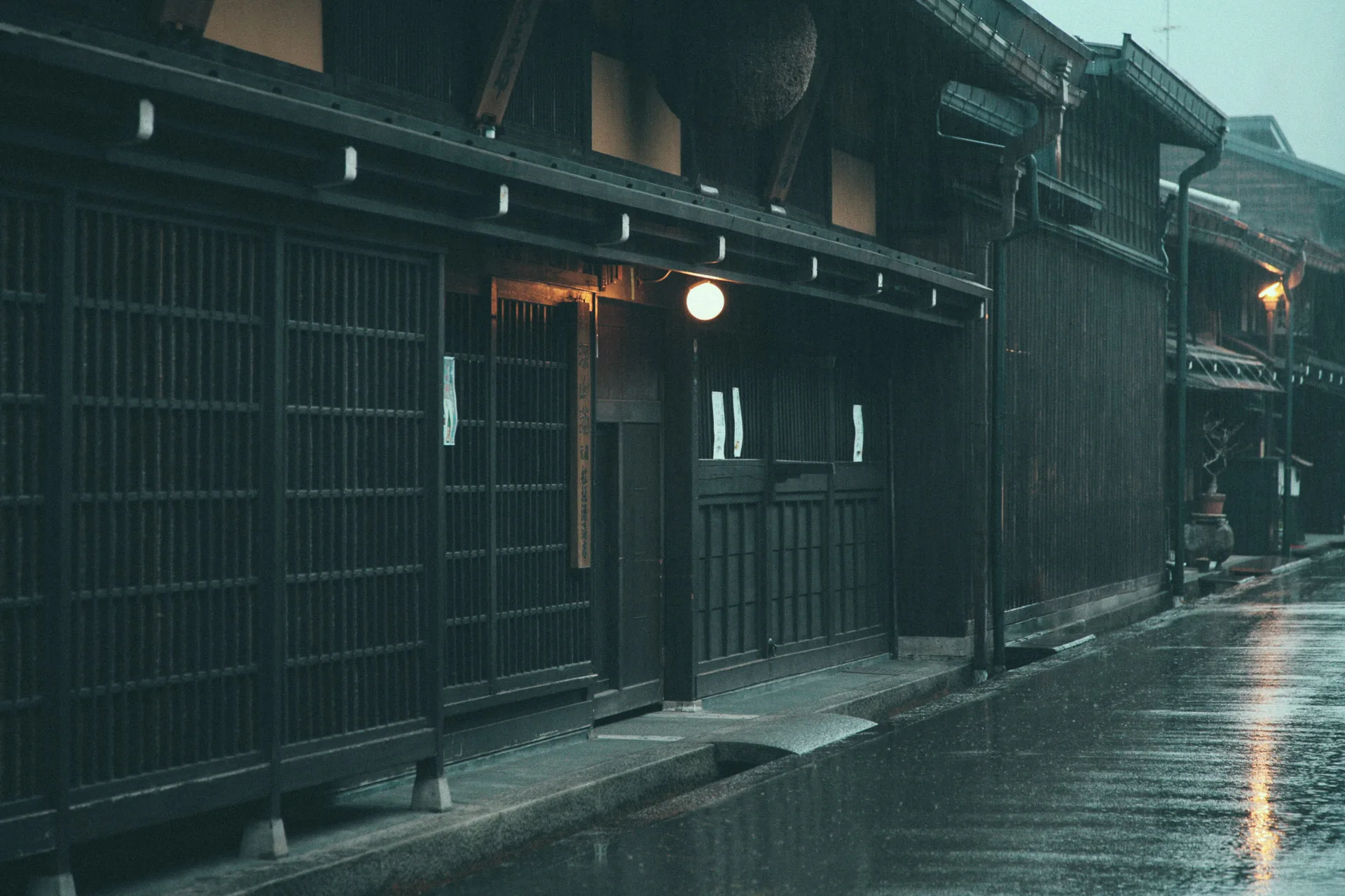 A lantern glowing beside latticed shop fronts on a wet street