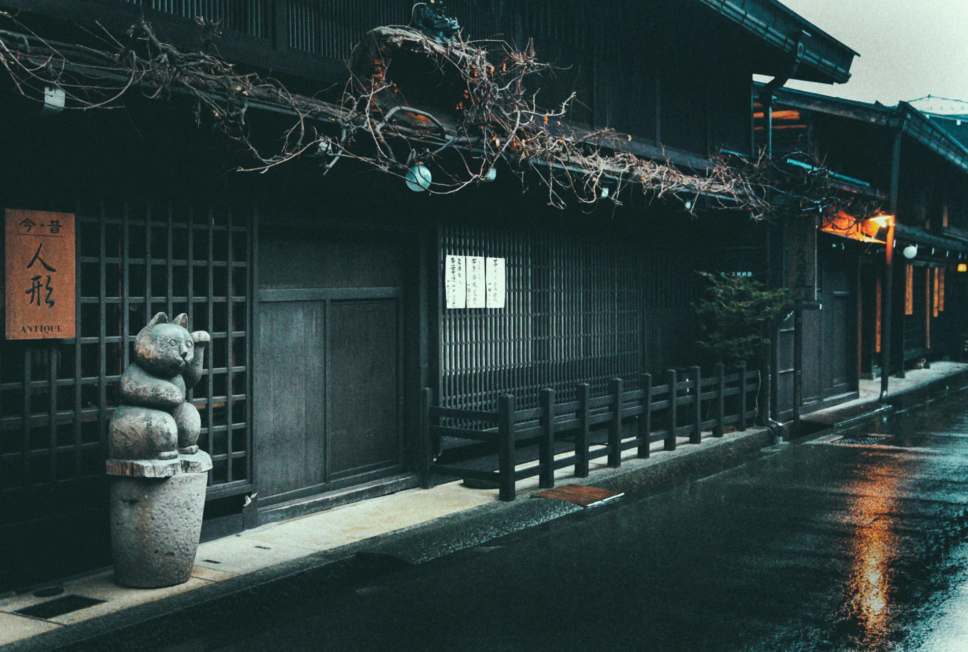 A stone maneki-neko beside a merchant house under bare vines