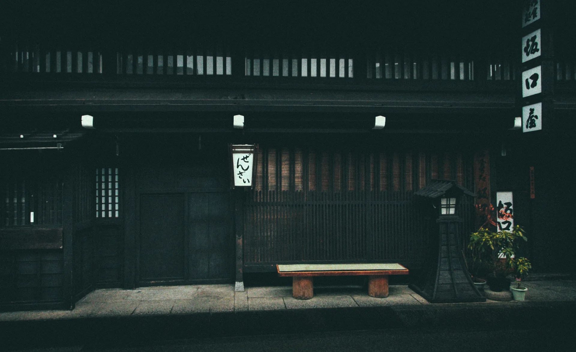 A wooden bench and lantern in front of a dark merchant house