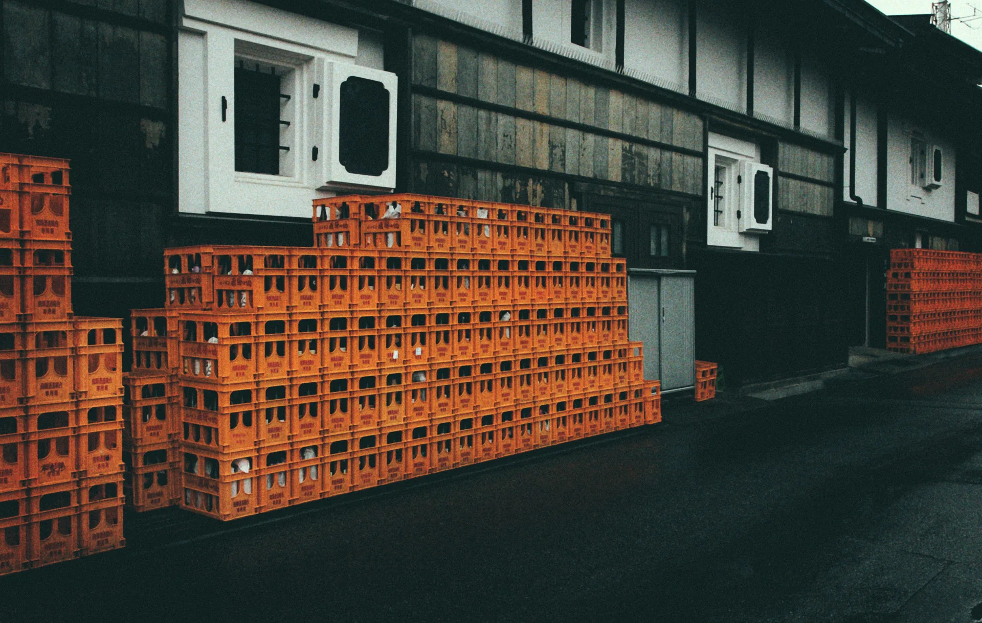 Orange sake crates stacked against a wooden storehouse