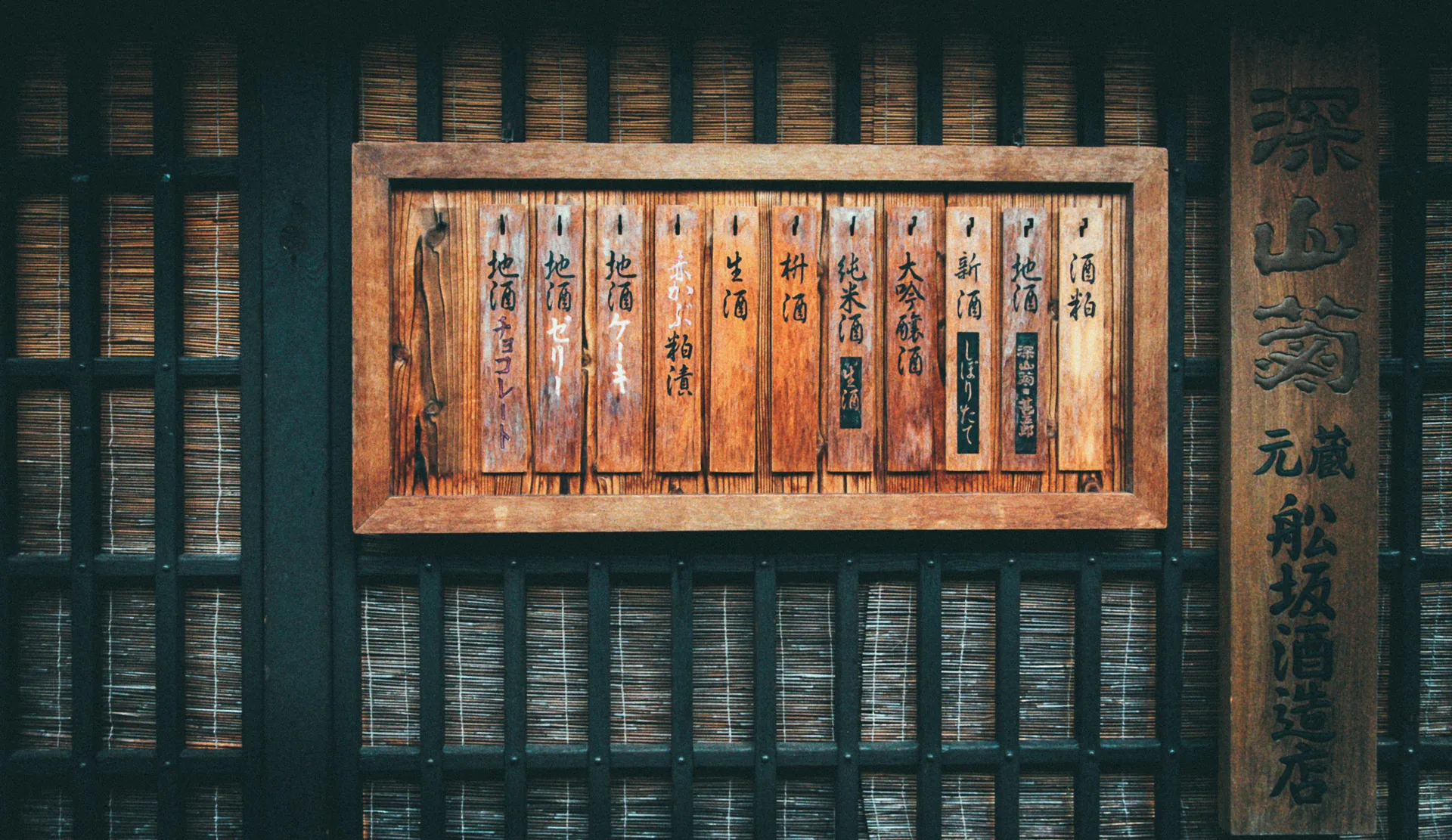 A wooden menu board of sake names on a latticed wall