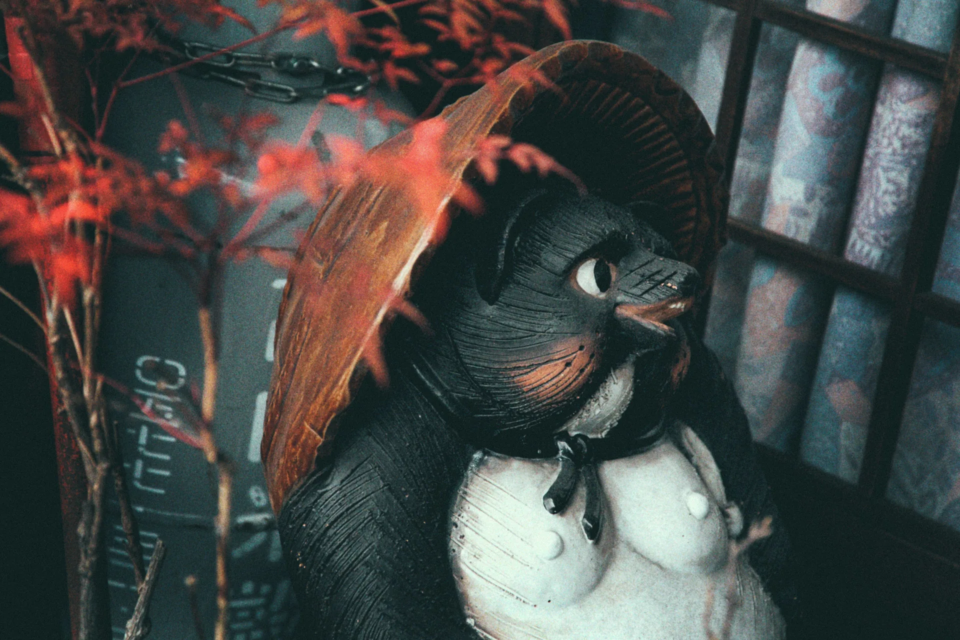 A tanuki statue under a straw hat beside red maple leaves