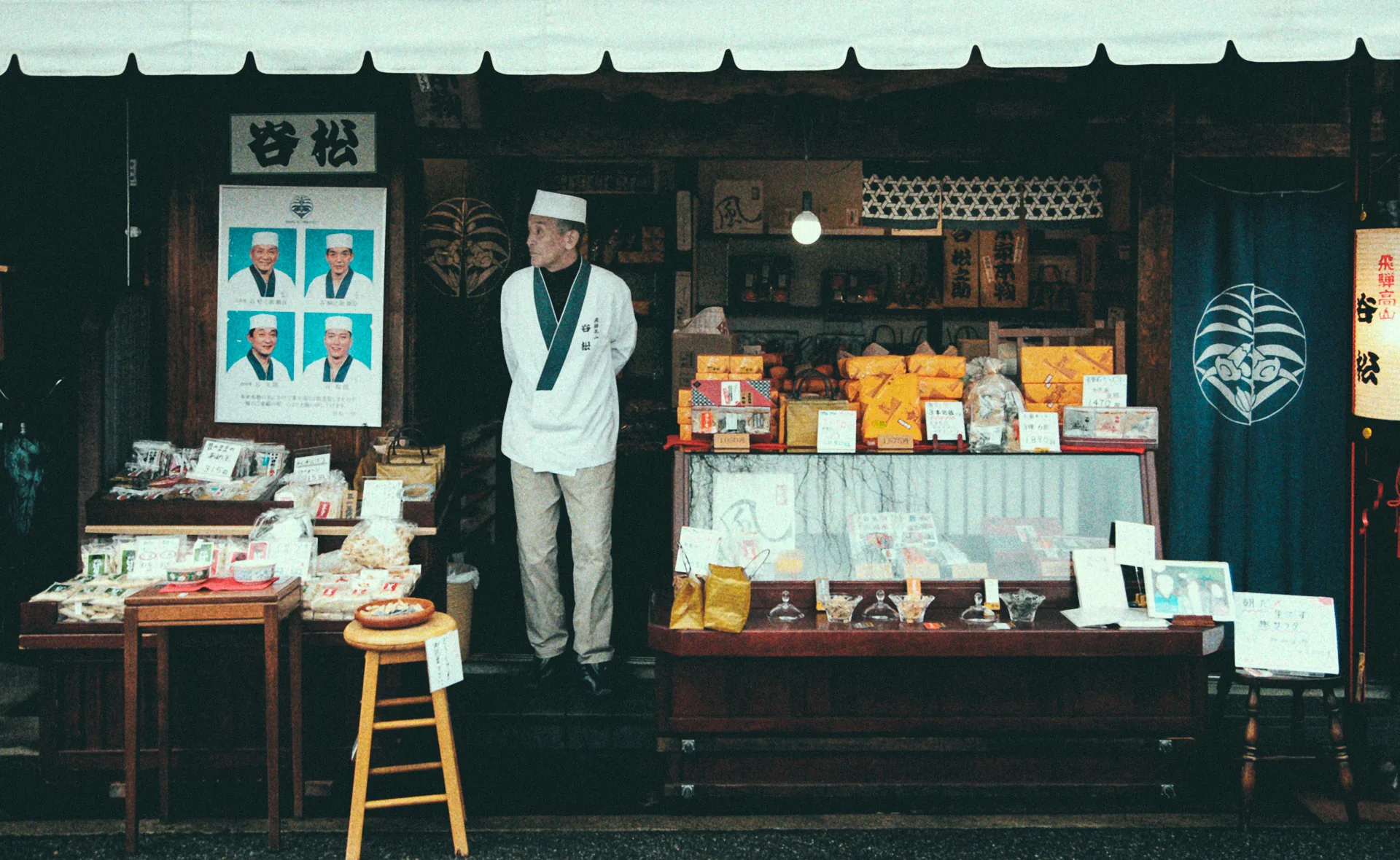 A shopkeeper in white standing at the door of a sweets shop