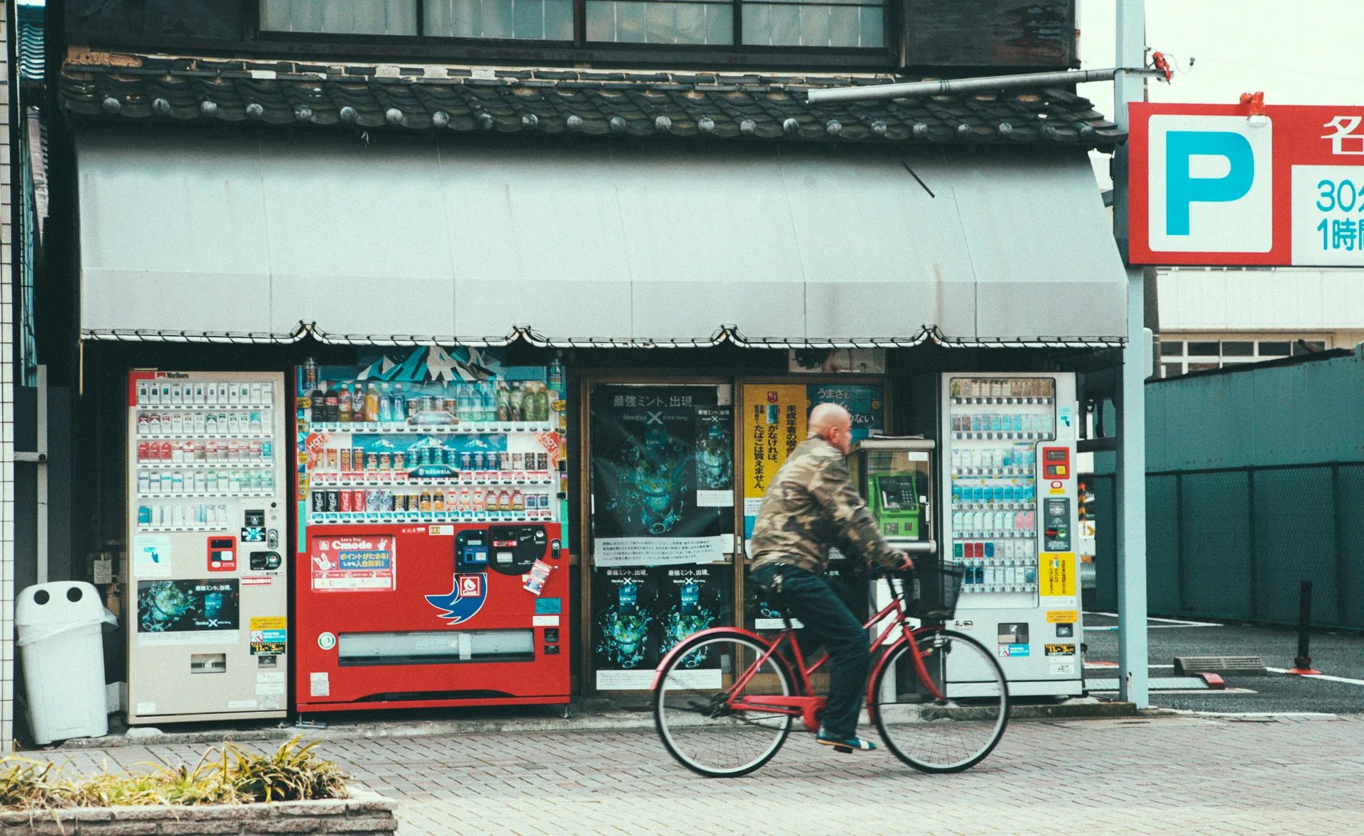 A man cycling past vending machines and a parking sign