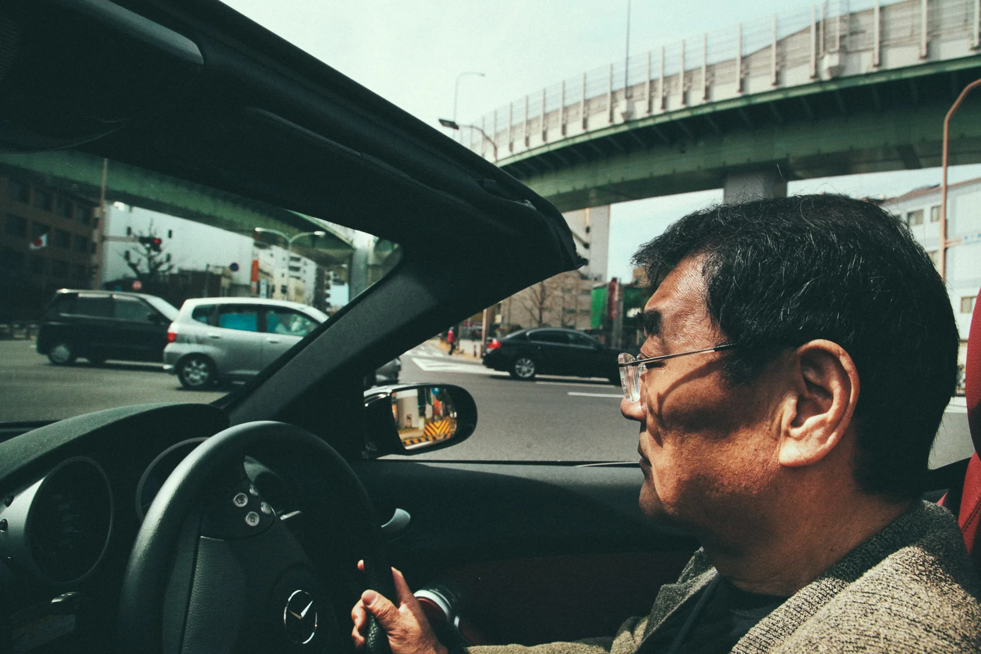 Masao driving his convertible under an elevated expressway