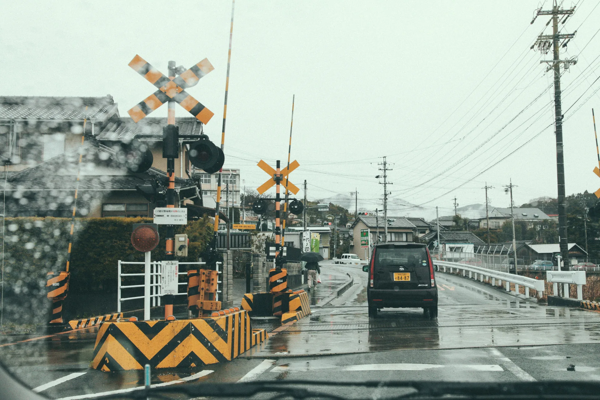 A rainy railway crossing seen through the windshield
