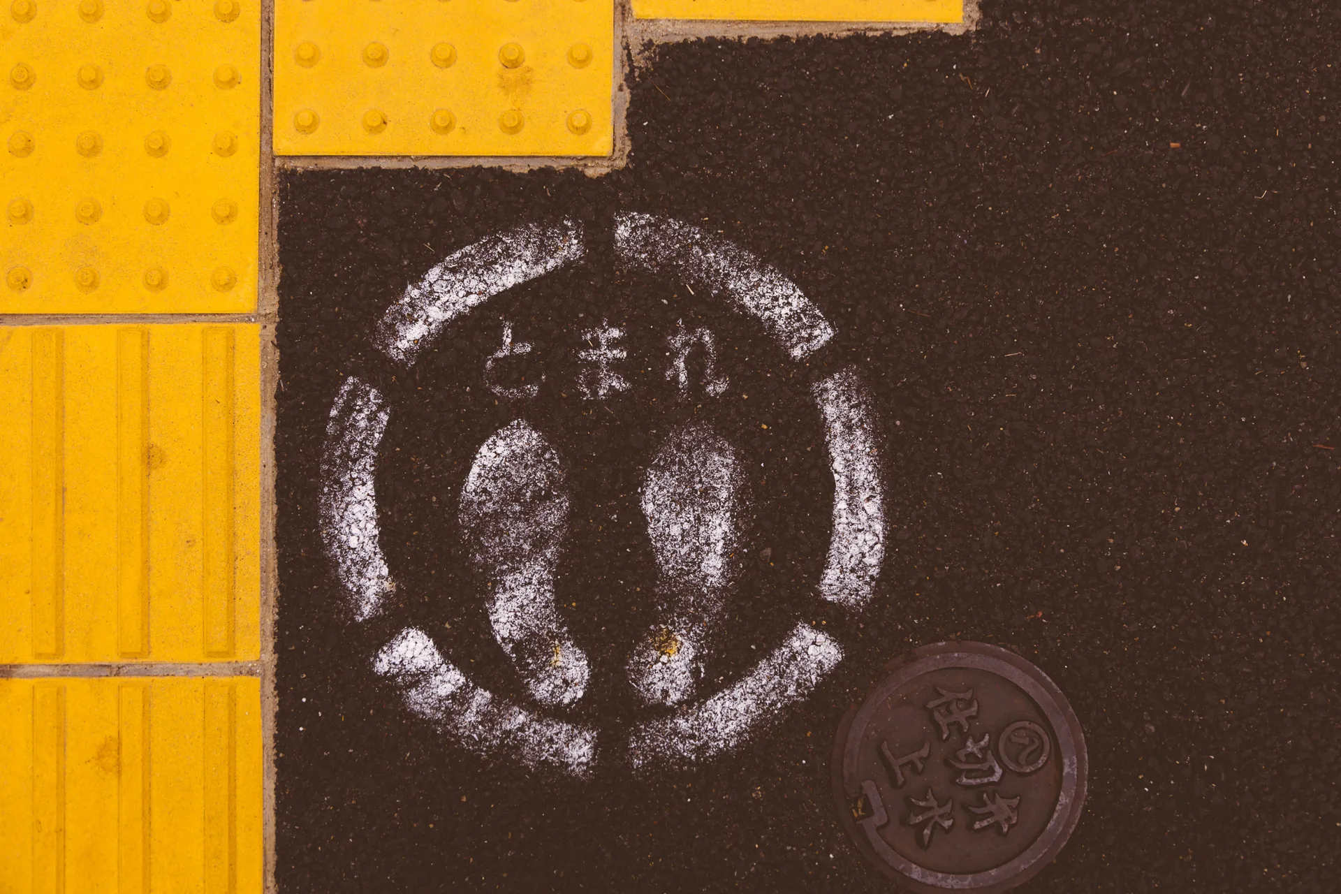 A painted stop sign on the road beside yellow tactile paving