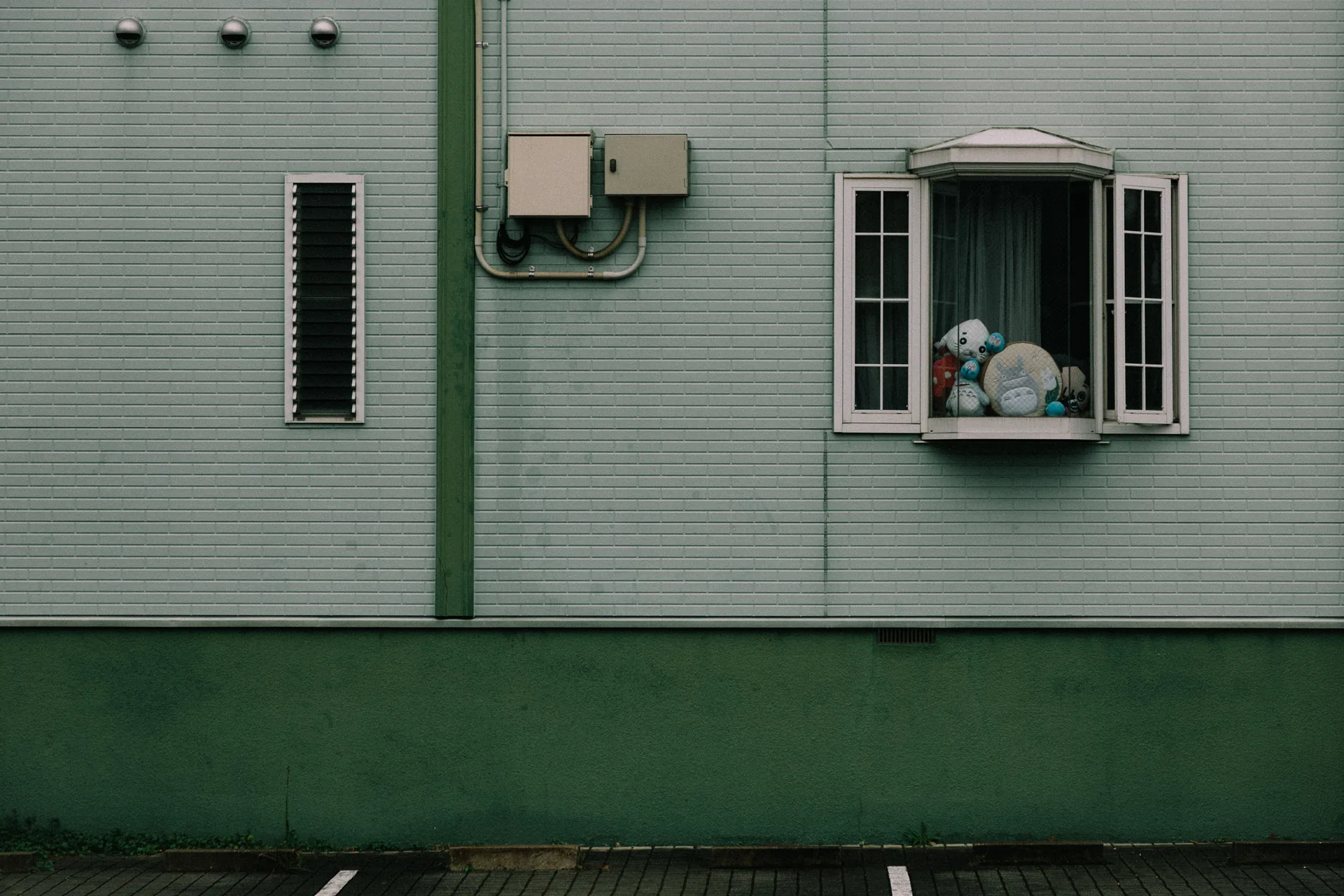A Totoro figure peering from a small window in a green wall