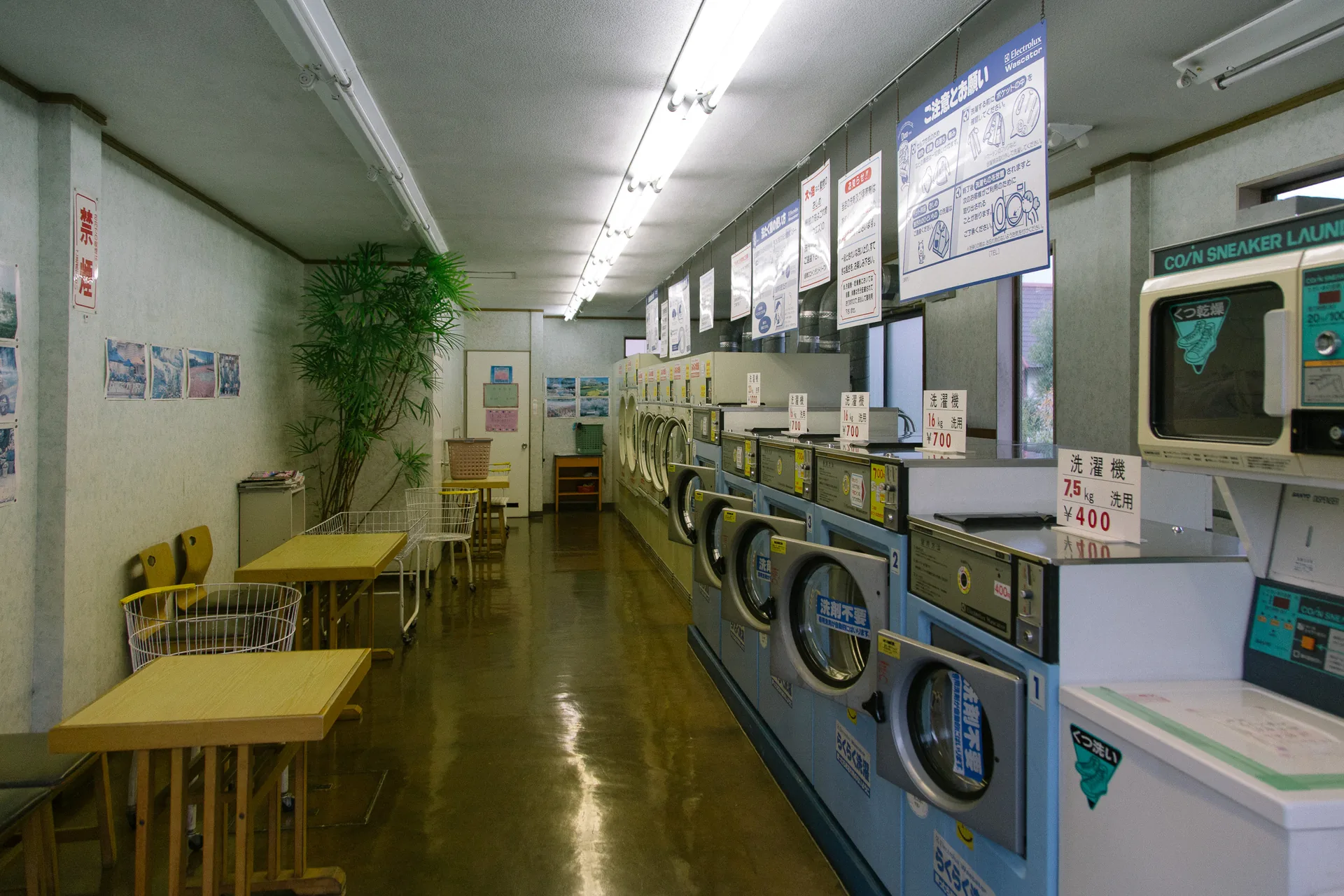 A long laundromat with yellow tables and rows of machines