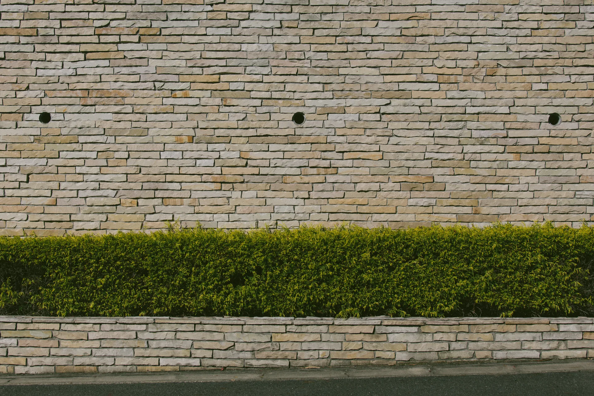 A stone-clad wall above a trimmed hedge