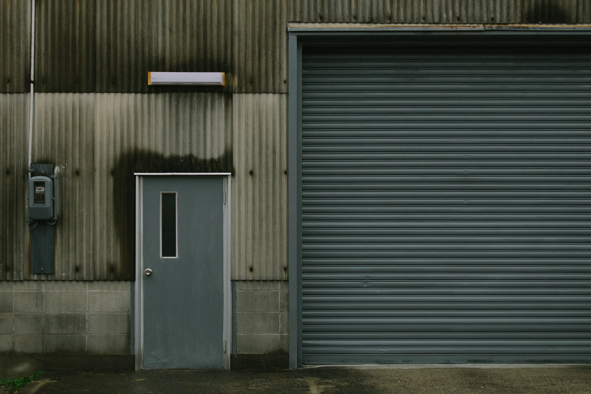 A metal door and a closed shutter under a lamp