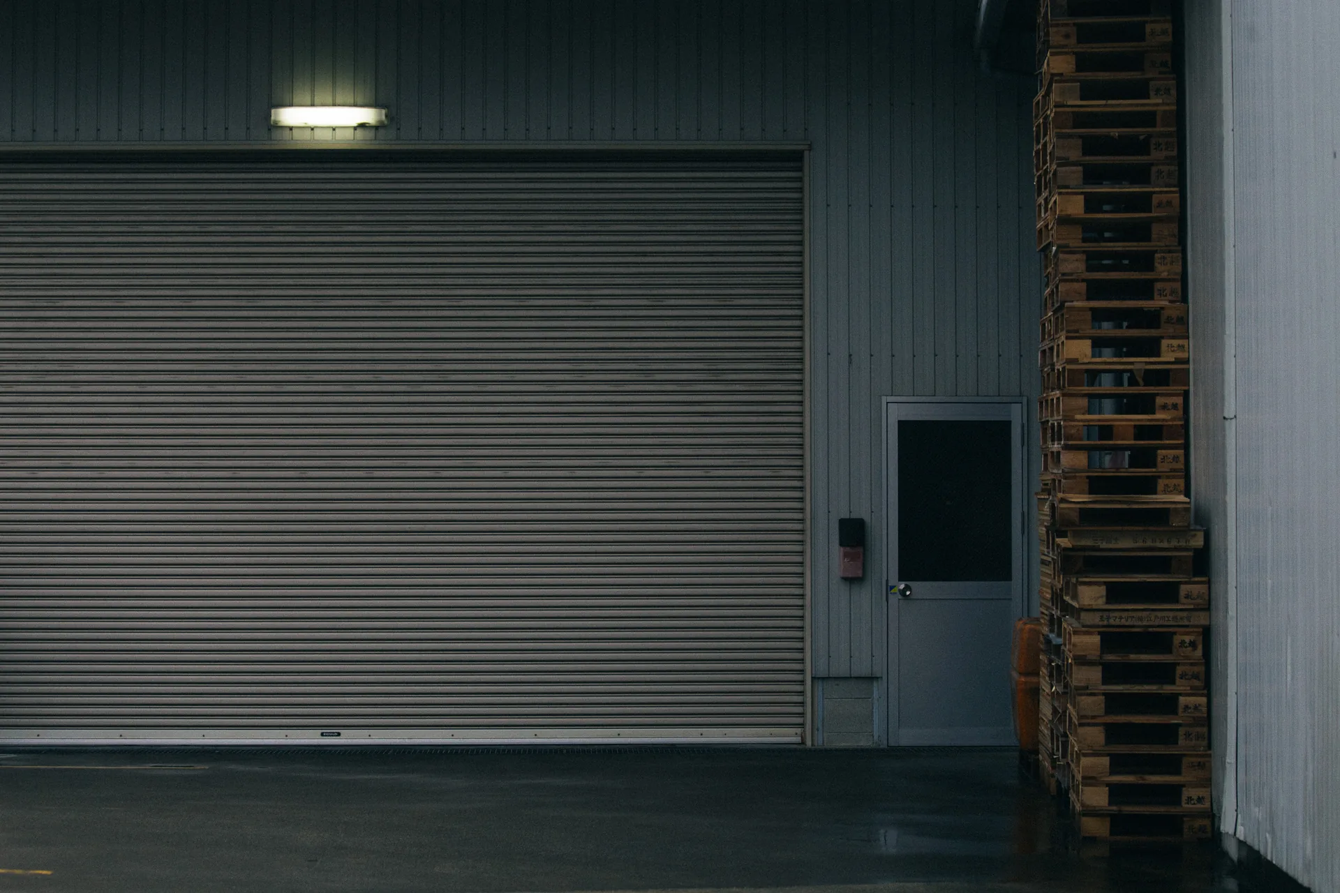 A metal door under a light, with stacked pallets