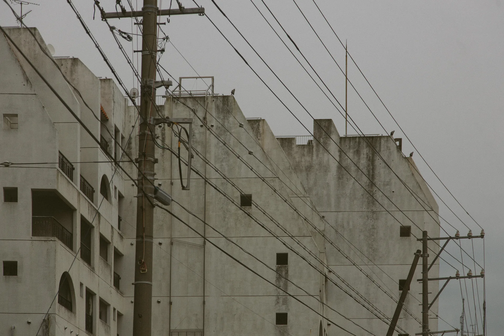 A grey building behind utility poles and wires