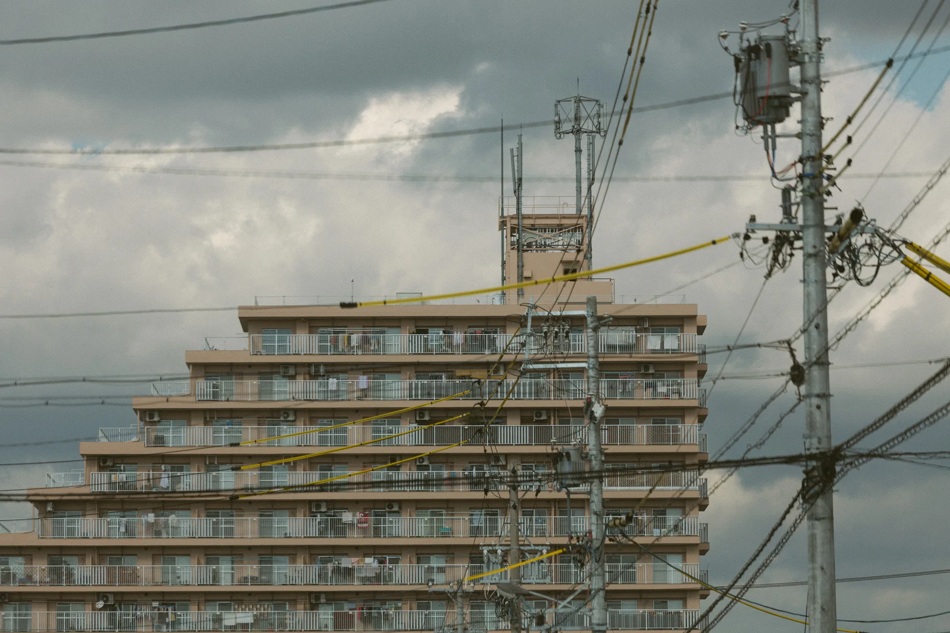 A stepped apartment building behind wires and clouds