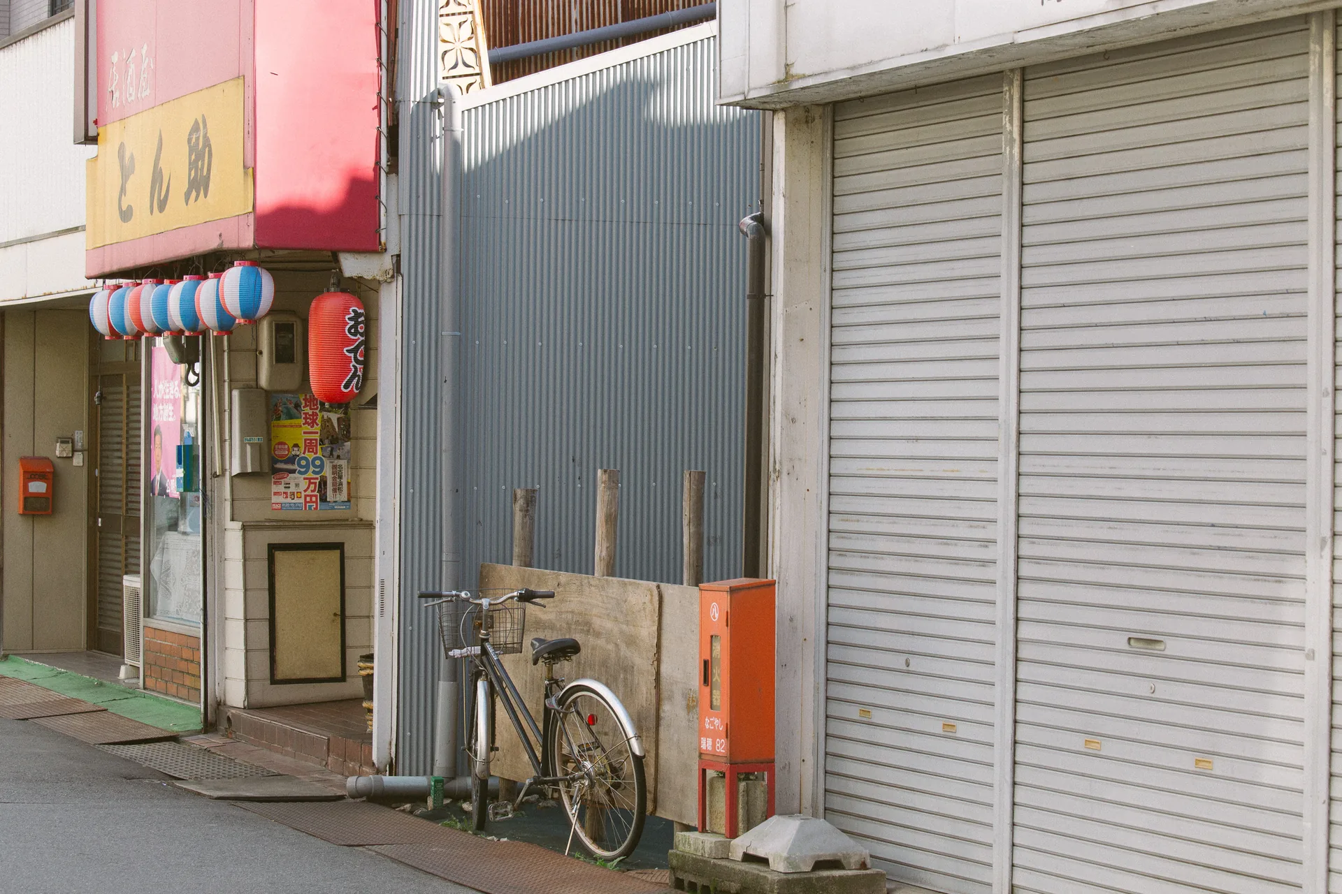 A small shop with lanterns and a bicycle by closed shutters