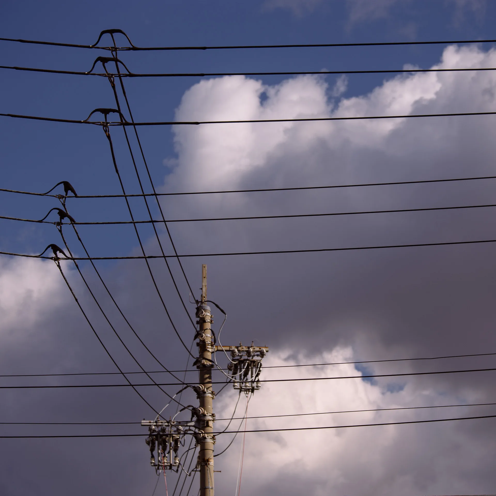 Wires meeting at a pole against blue sky and clouds
