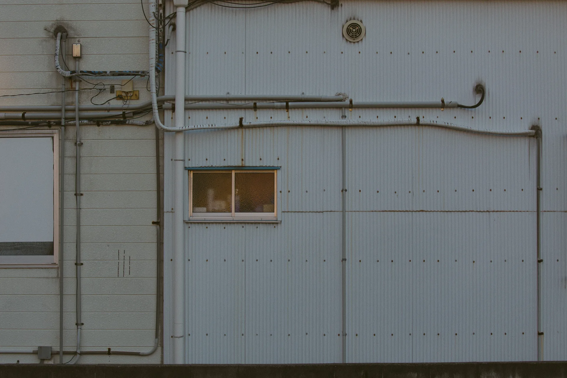 A small window among pipes on a pale wall
