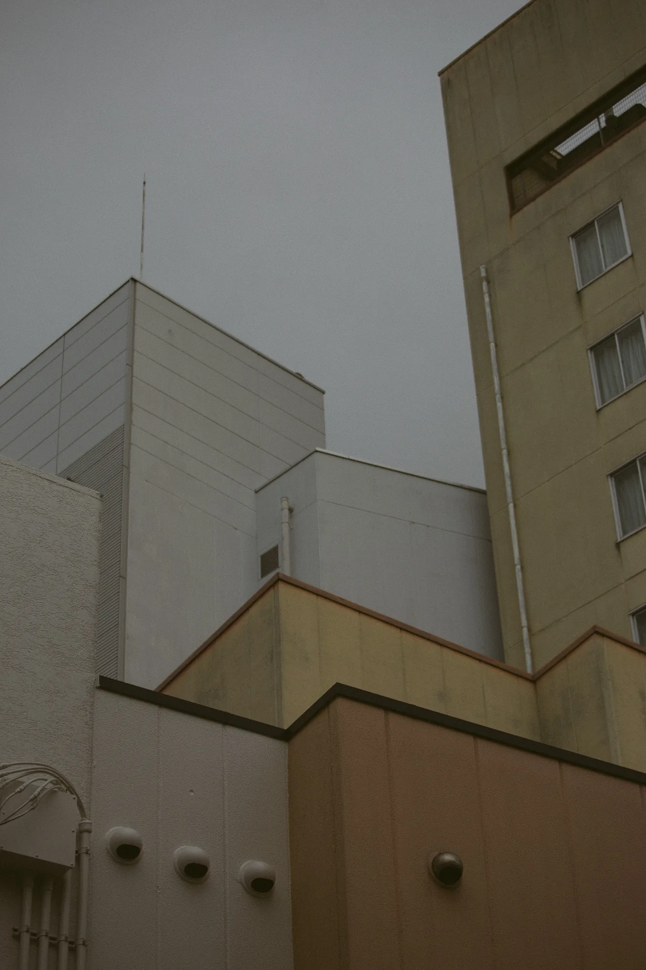 Pale and ochre buildings stacked against a grey sky, with round vents