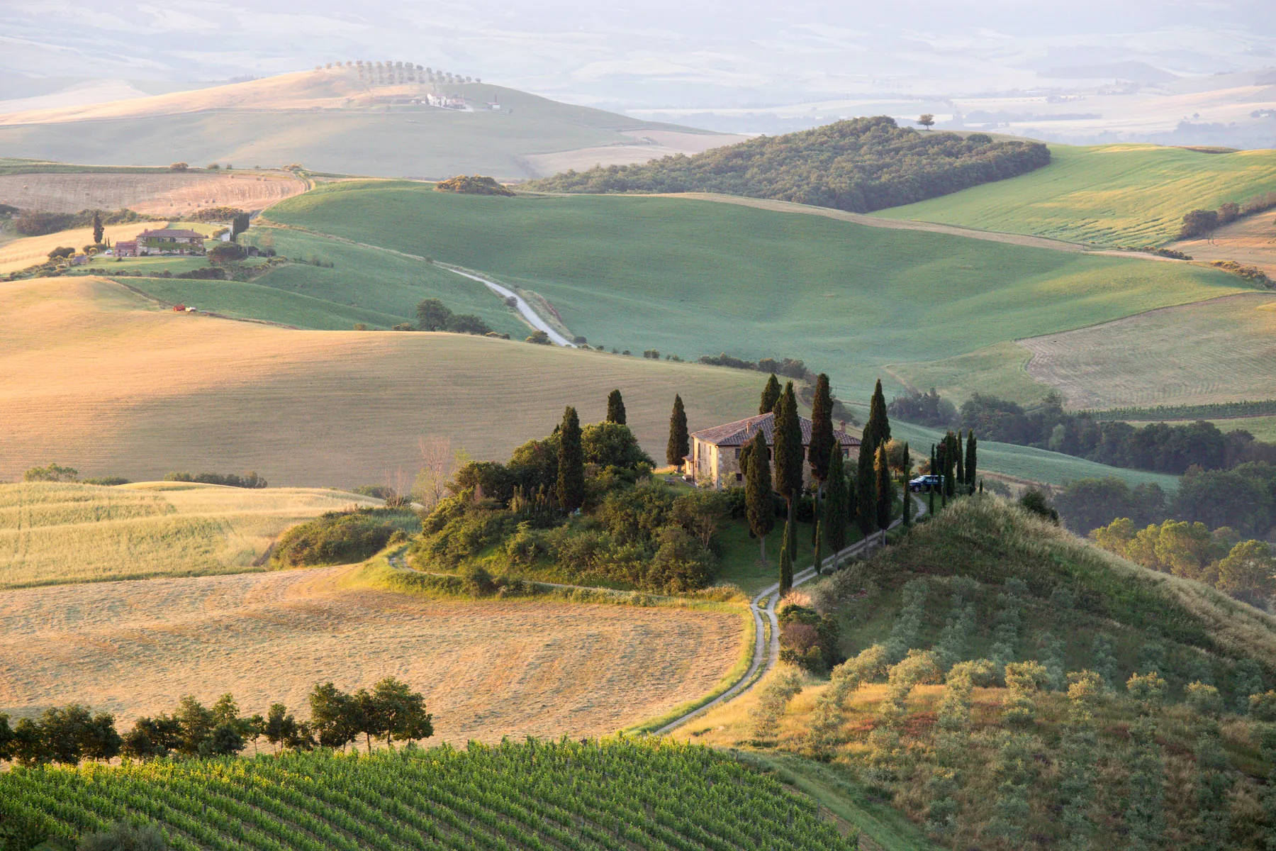 Farmhouse and cypresses on a knoll above a patchwork of fields and a winding road